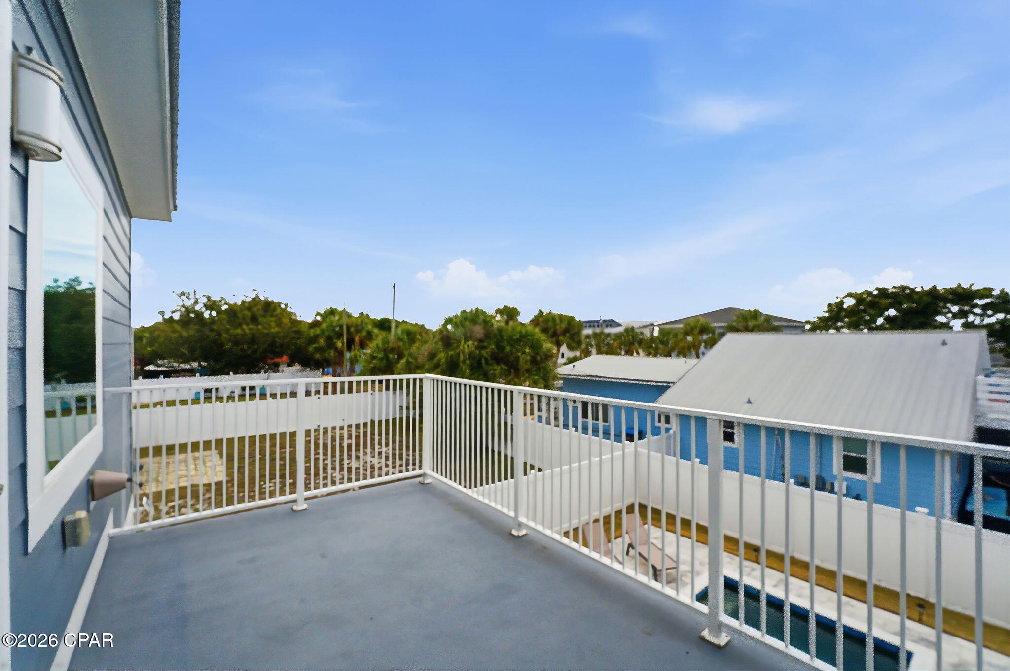 Elevated balcony with white railings overlooking nearby homes and a small pool.