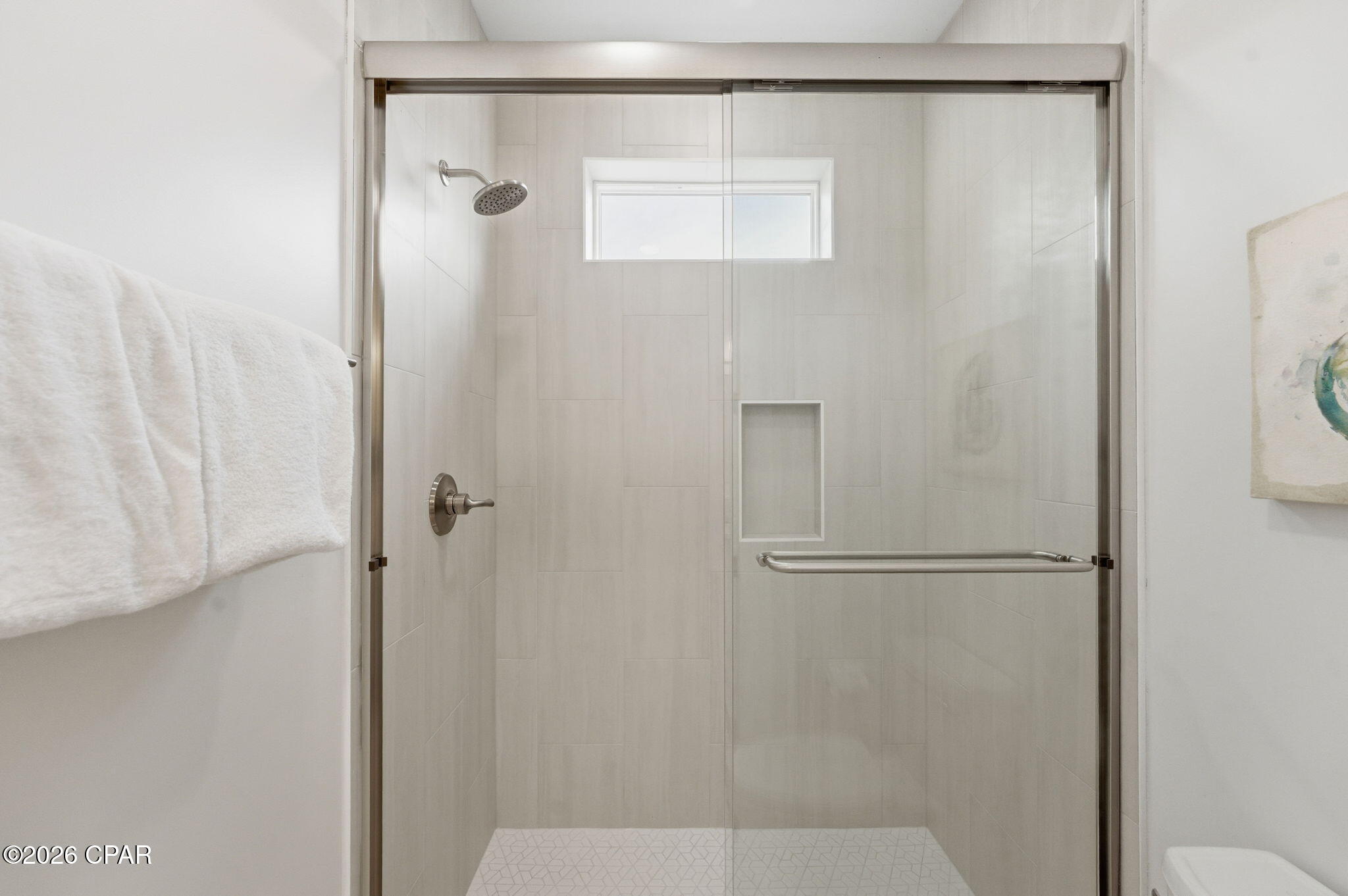 Walk-in shower with glass doors, light tile, a built-in niche, and a high window.
