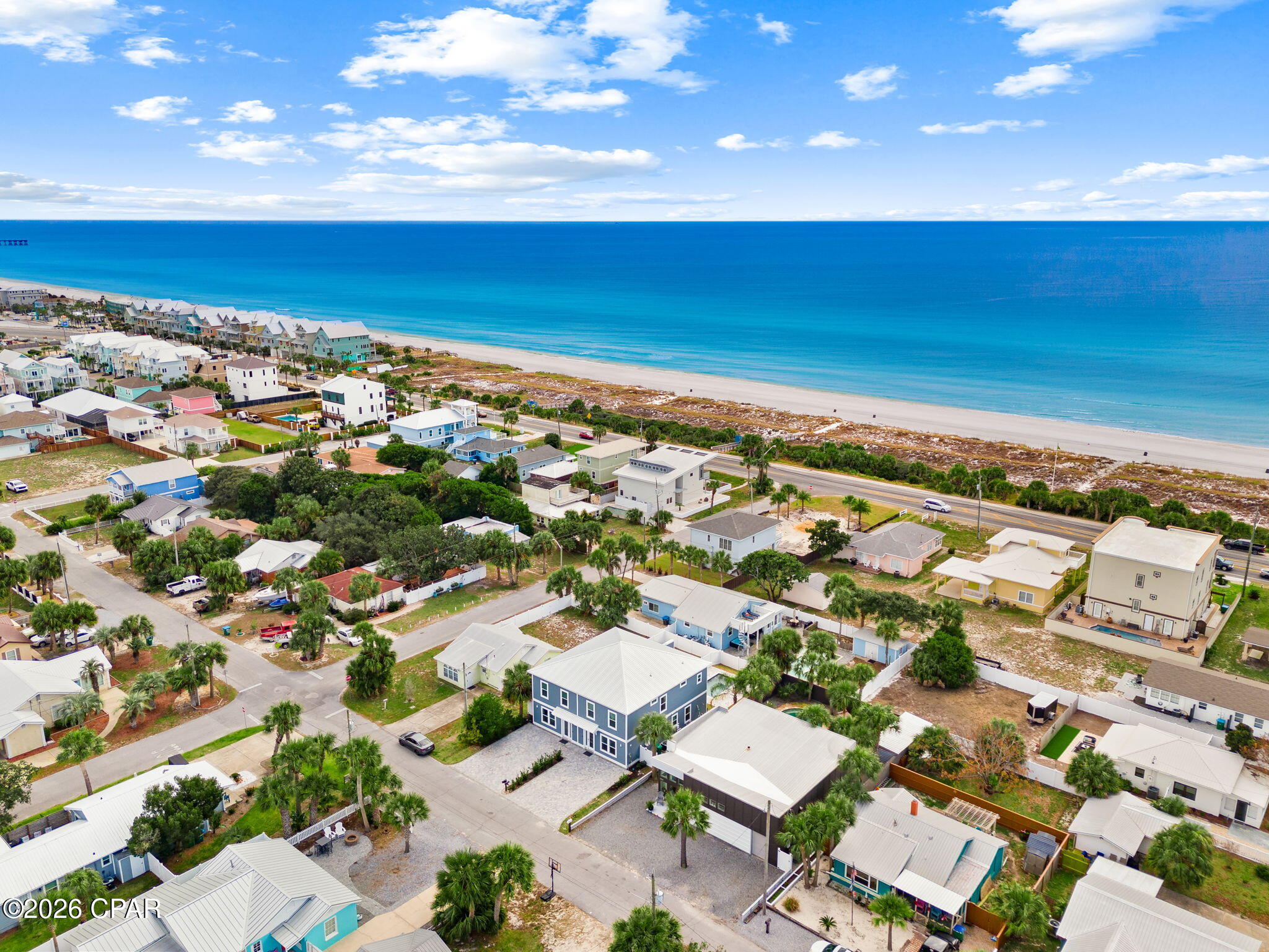 Aerial coastal neighborhood with a blue multi-unit home, sandy beach, and Gulf waters.