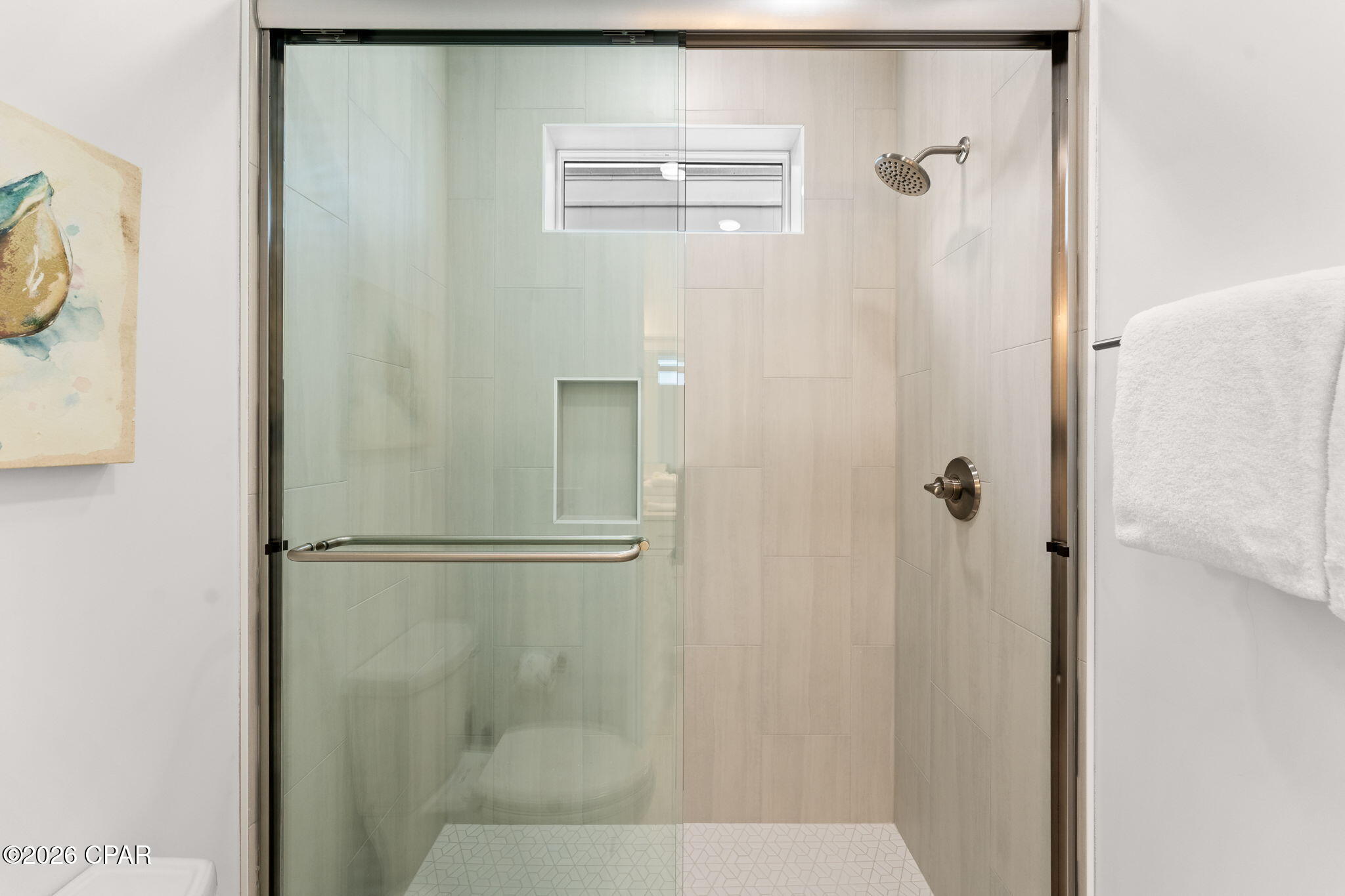 Walk-in shower with glass doors, light tile, a built-in niche, and a high window.