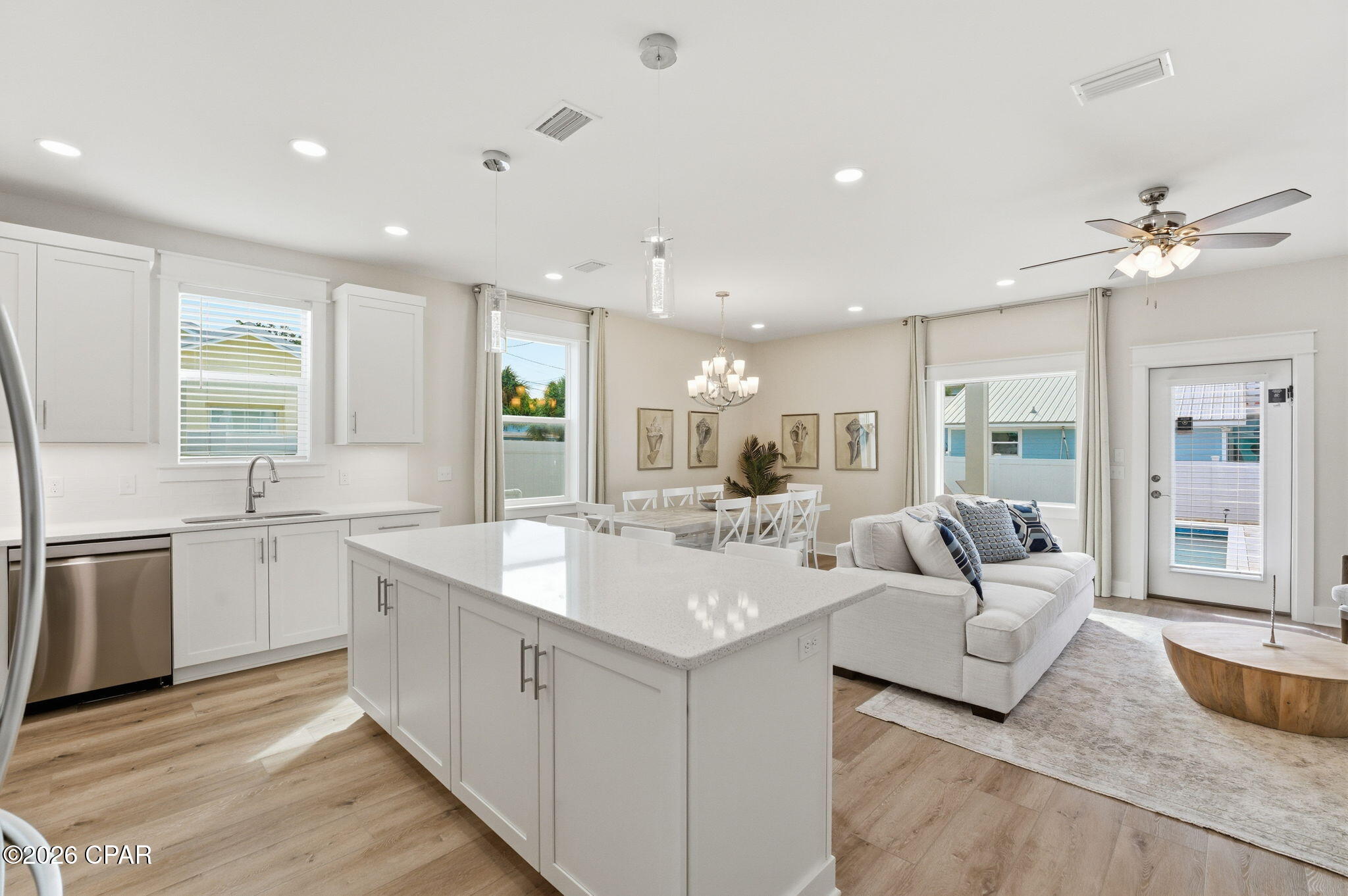 Open-plan kitchen and living area with a large white island, dining table, and white sectional sofa.