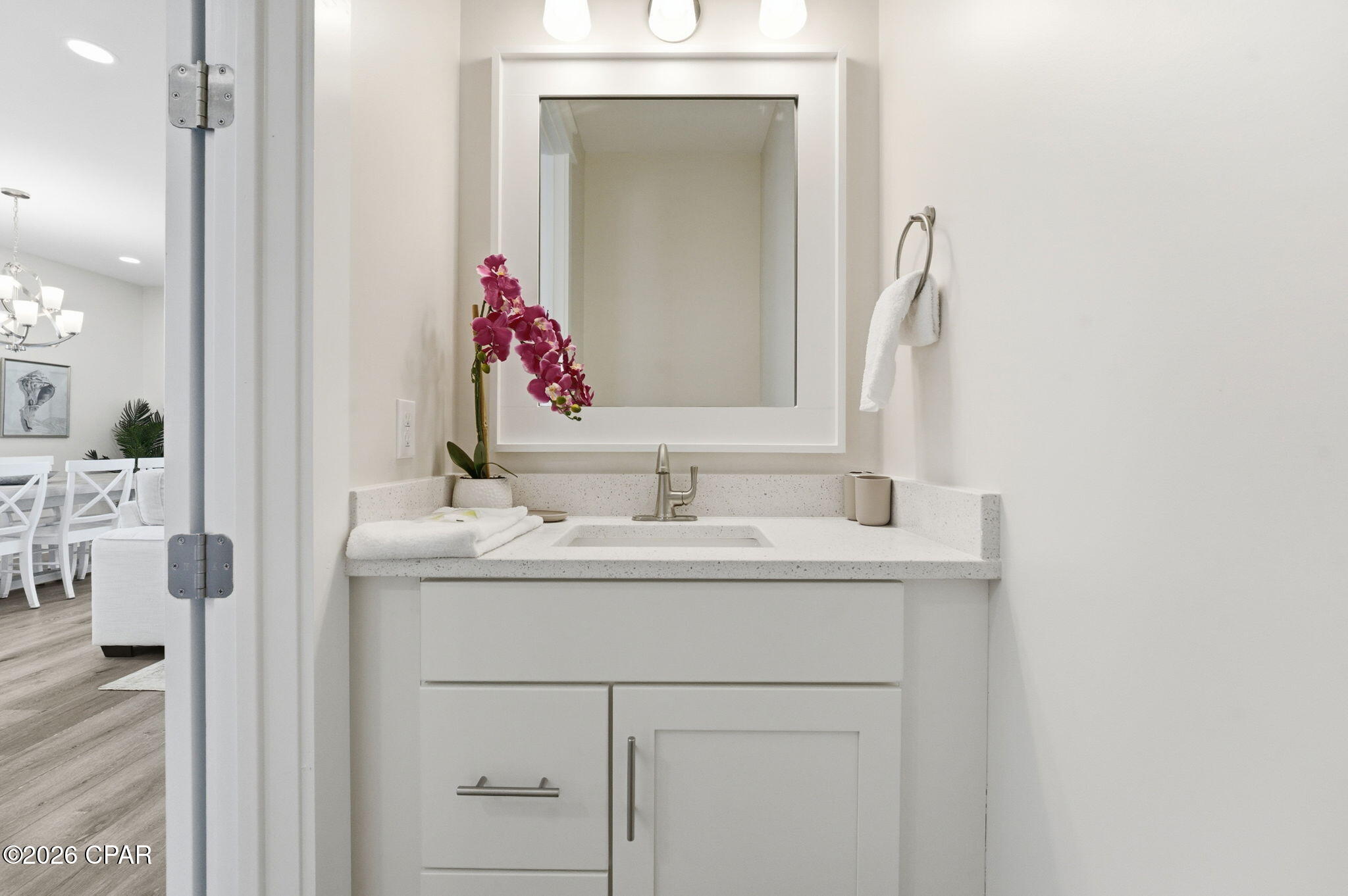 Bathroom vanity with a large mirror, white countertop, and pink orchid beside the sink.