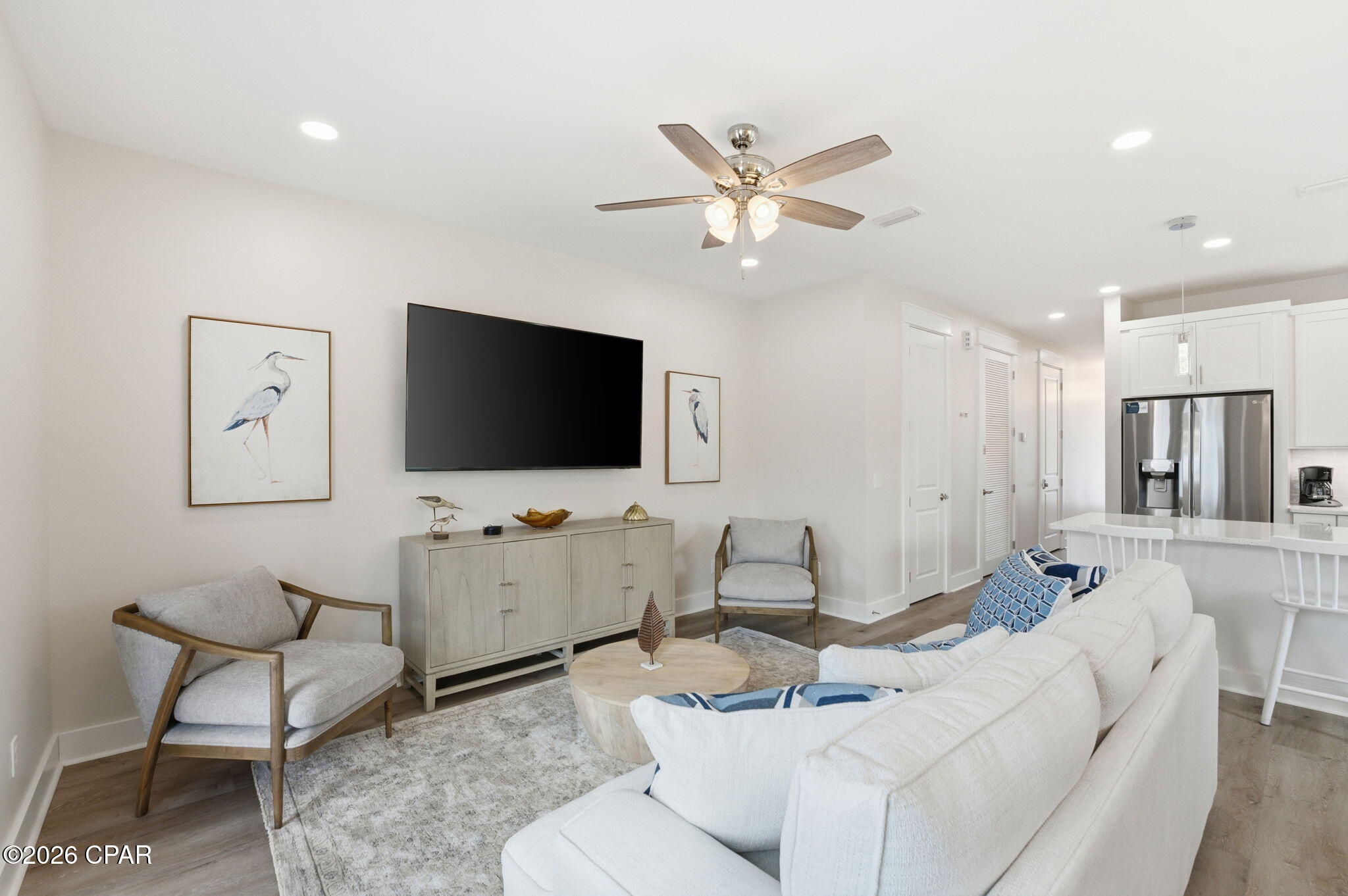 Living room with white sofas, coastal bird artwork, and an open kitchen.
