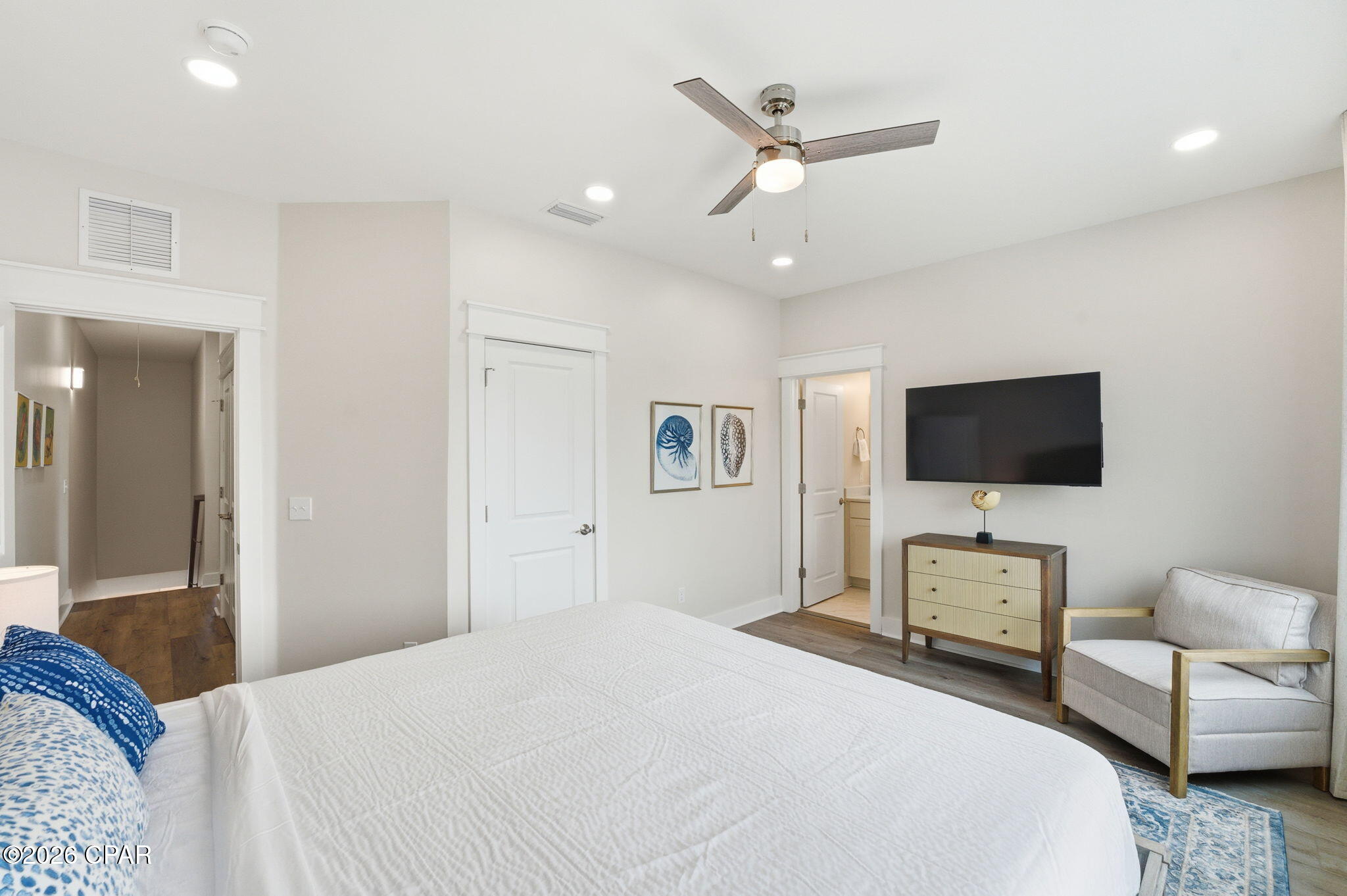 Furnished bedroom with a large white bed, blue accents, ceiling fan, and wall-mounted television.