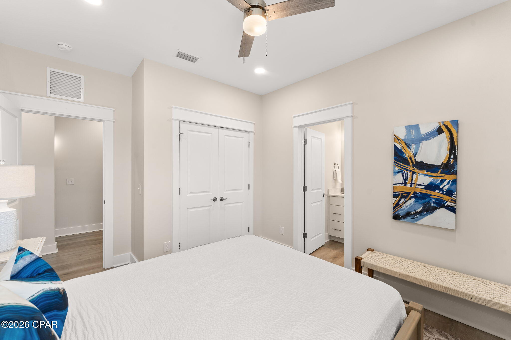 Furnished bedroom with white bed, double closet doors, and an open bathroom doorway.