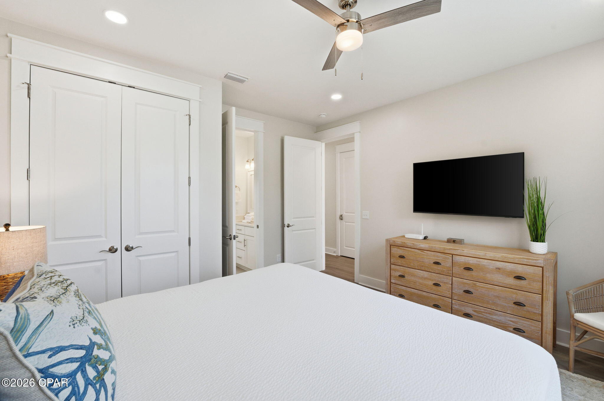 Bedroom with a white bed, wall-mounted television, and wooden dresser.