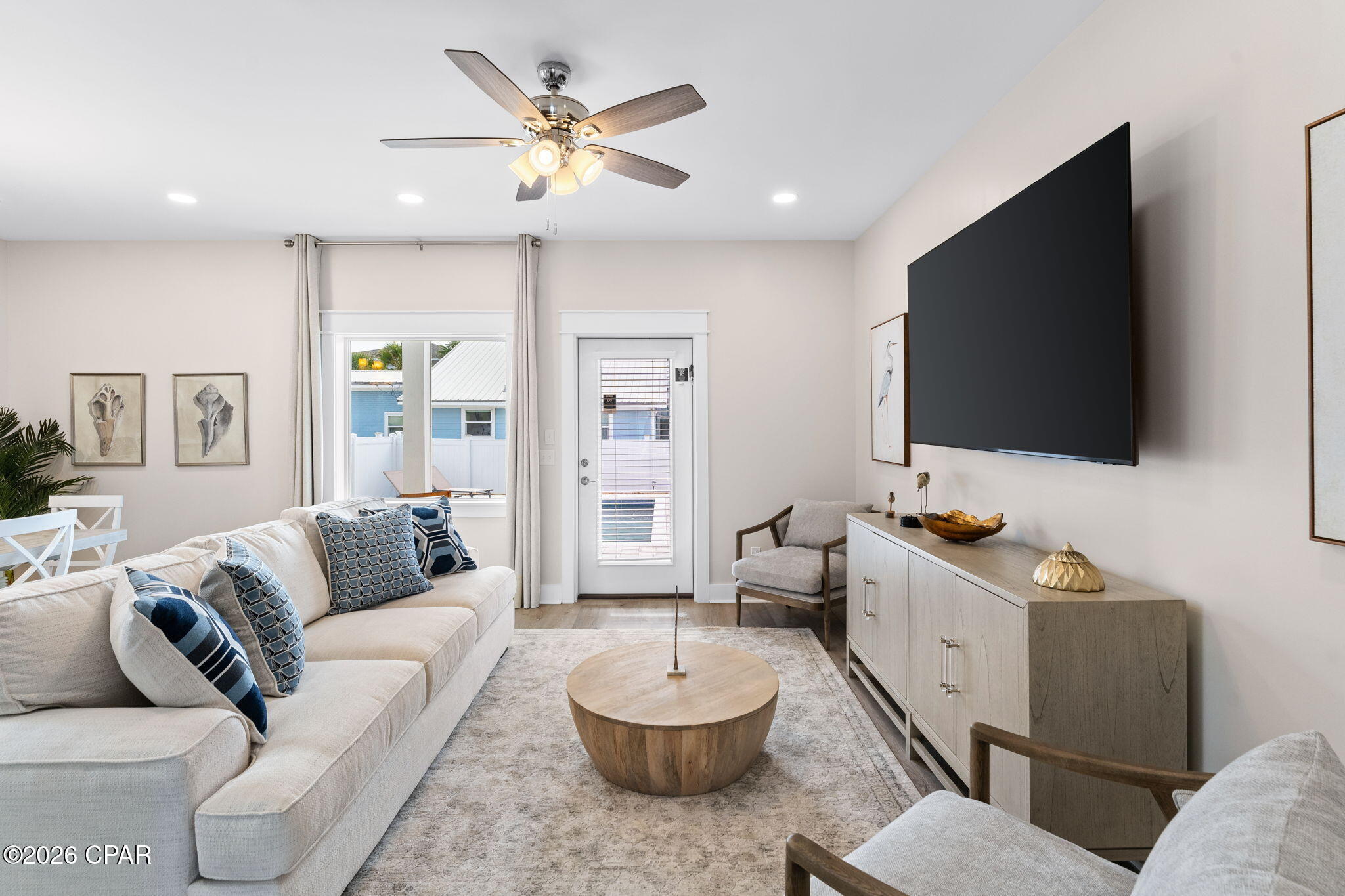 Furnished living room with a white sectional, round wood coffee table, and large wall-mounted television.