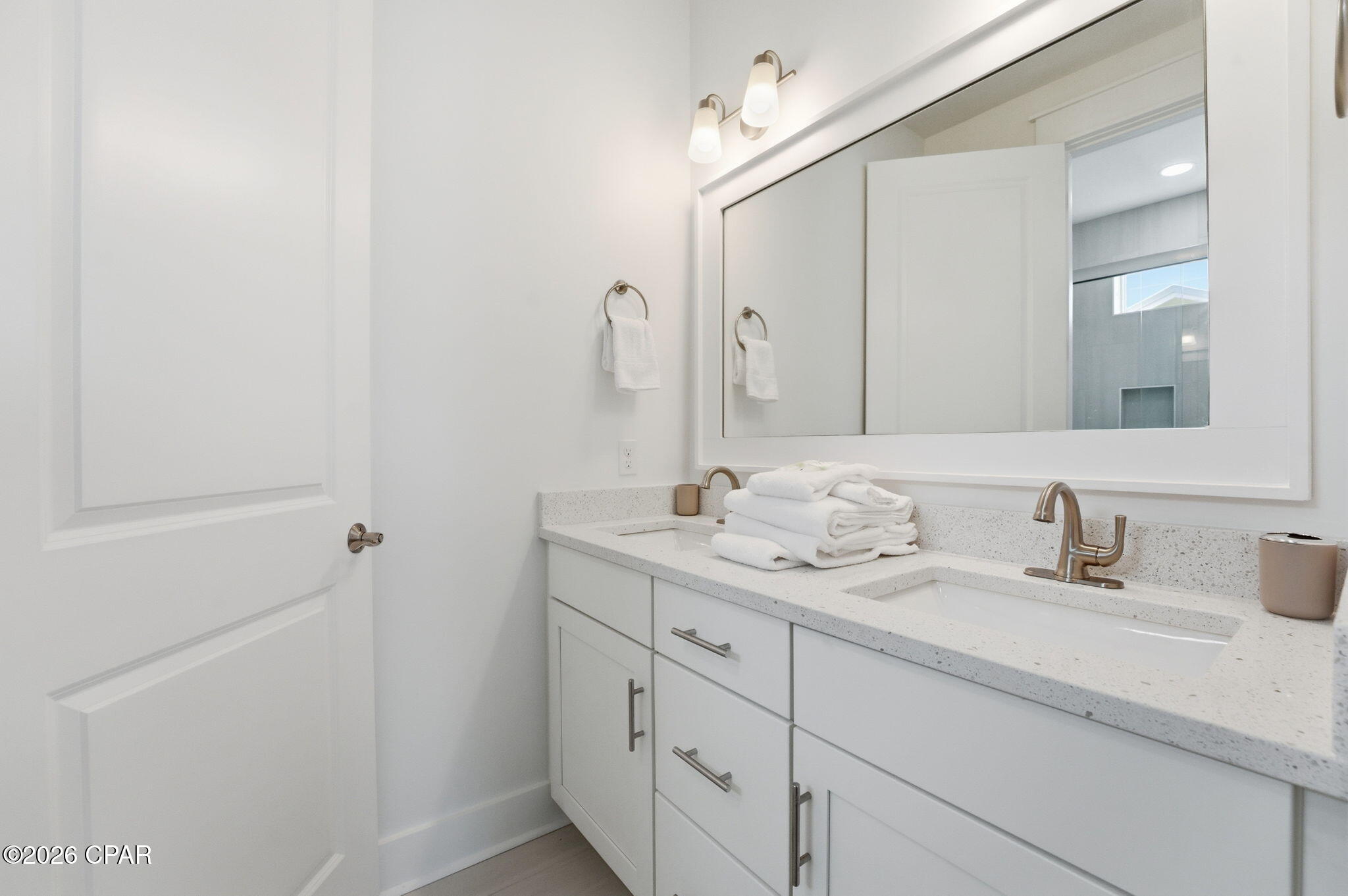 Bright bathroom vanity with double sinks, white cabinetry, speckled countertop, and a large mirror.