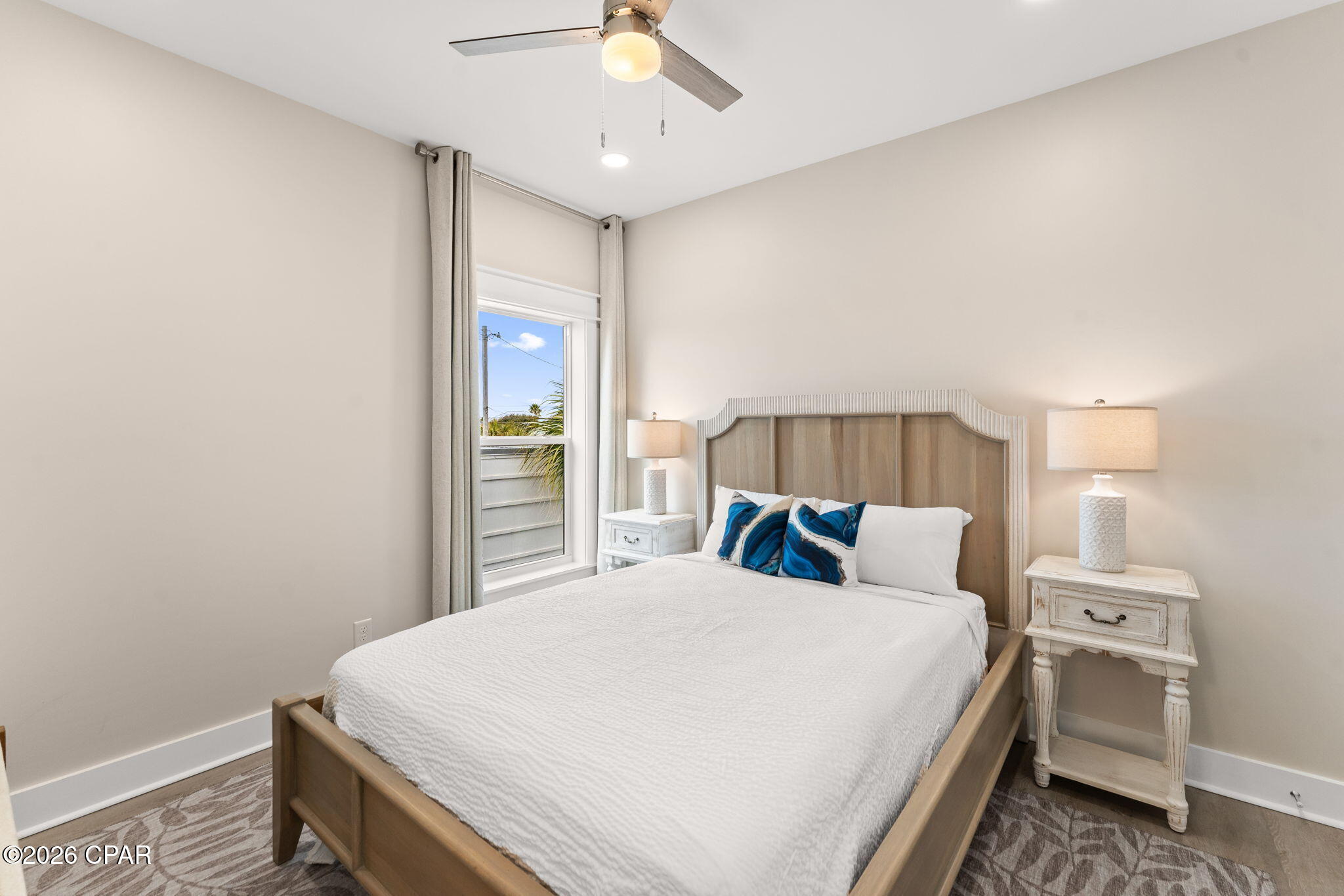 Bedroom with a wooden bed, blue accent pillows, matching bedside tables, and a curtained window.