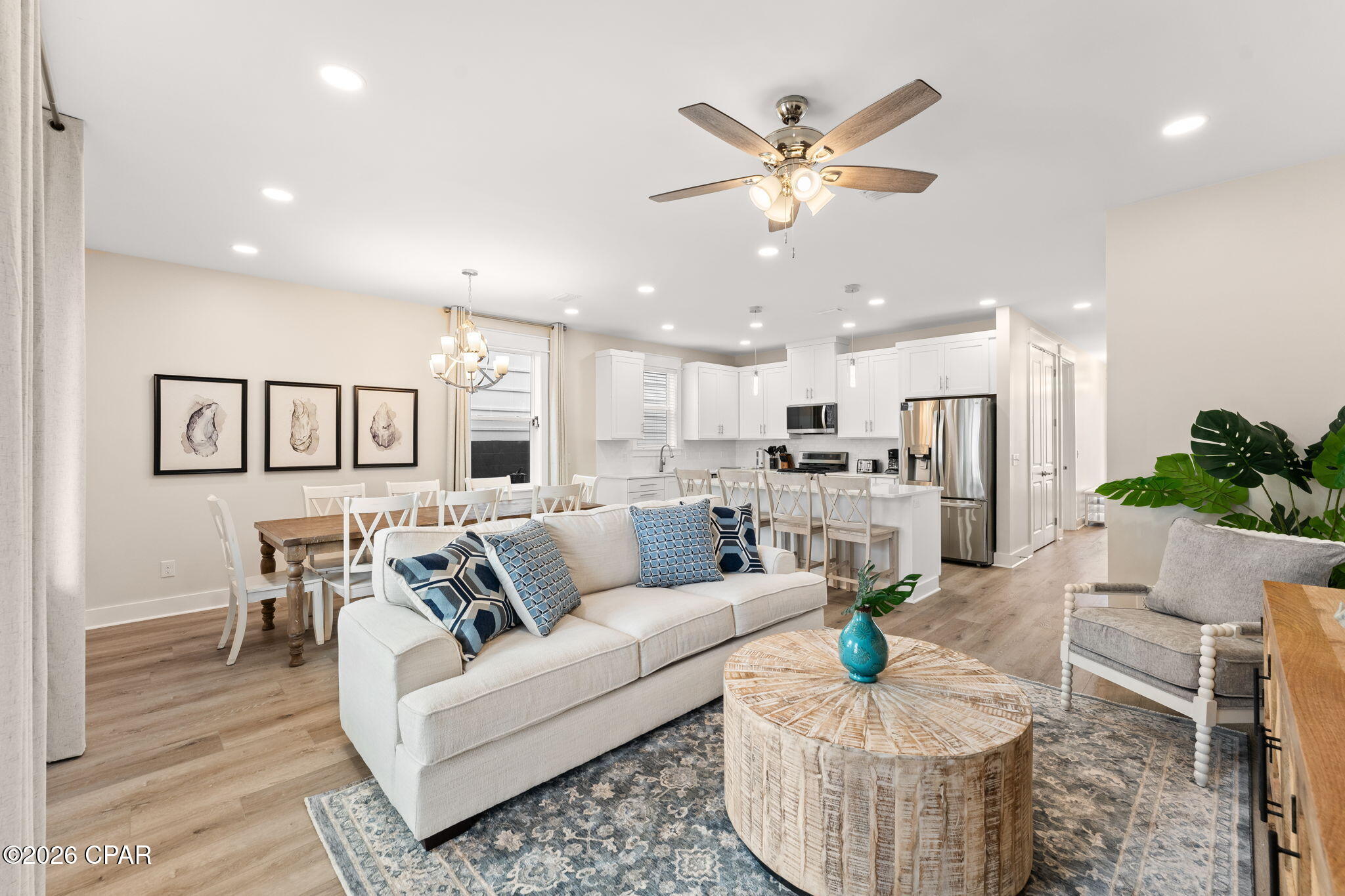 Open-plan living room with a cream sofa, round wood coffee table, and white kitchen.