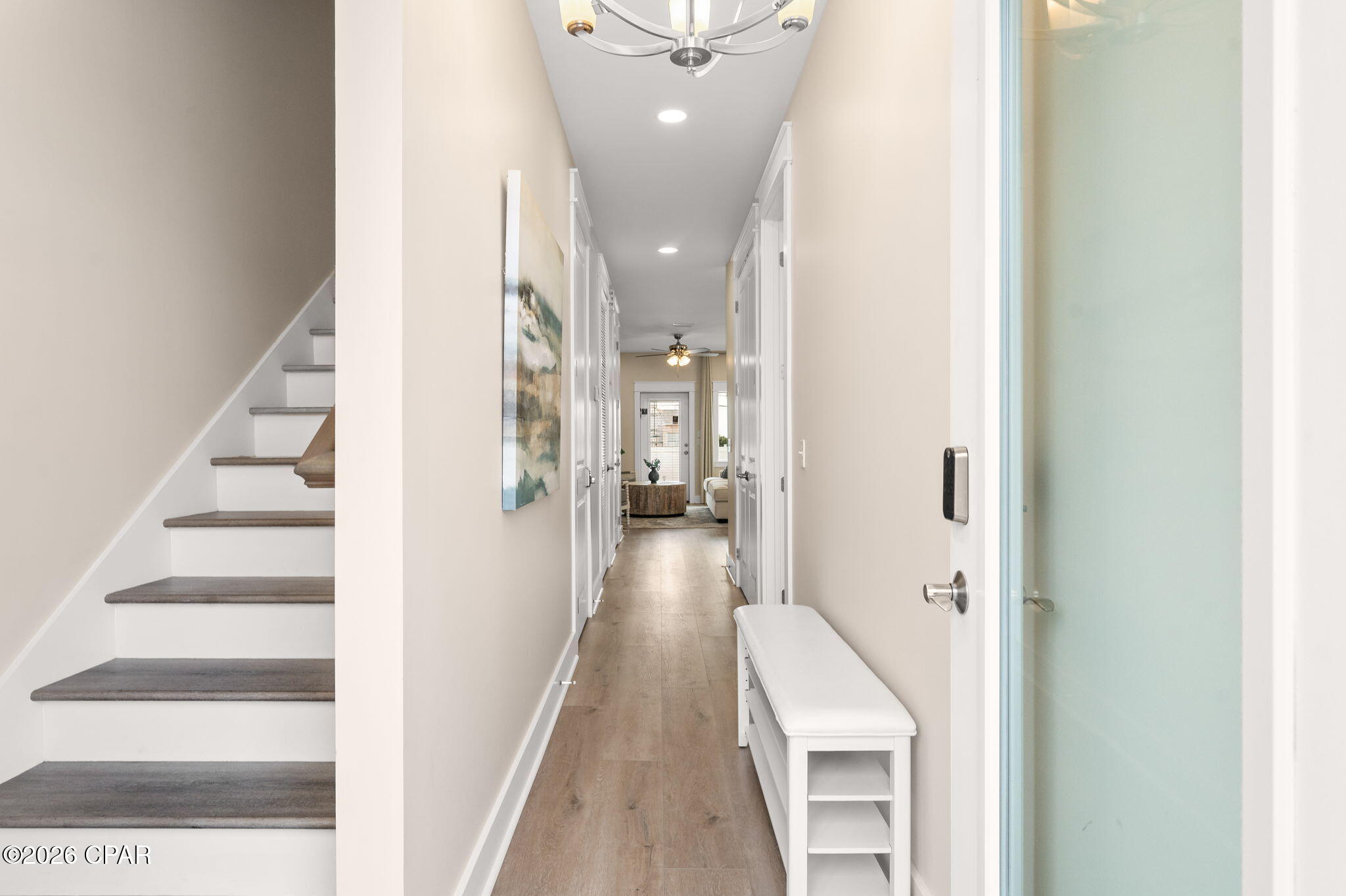 Entry hallway with a staircase, wood flooring, white bench, and frosted glass door.