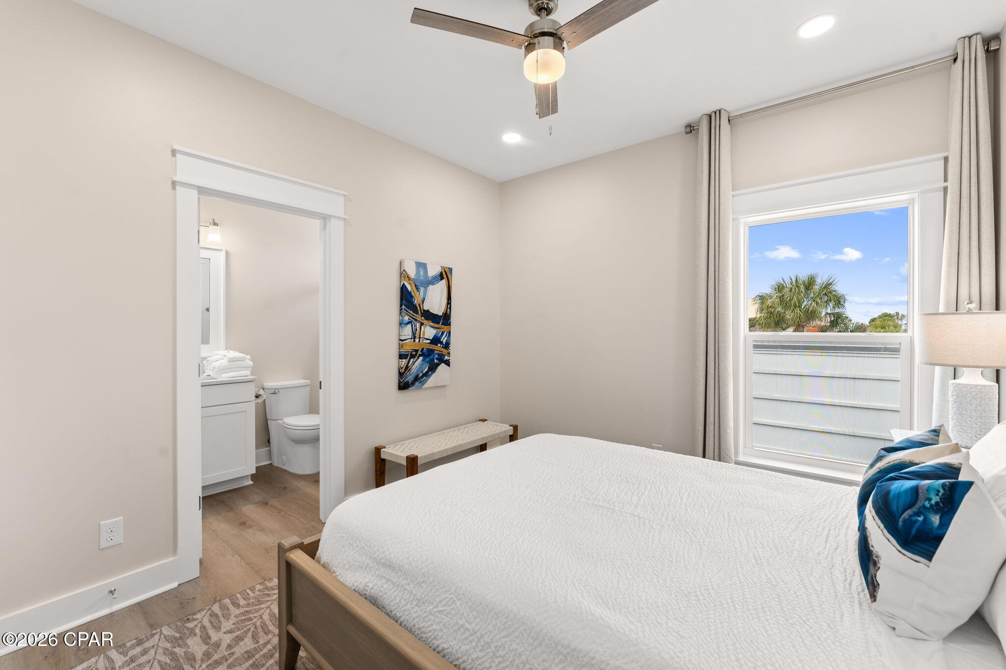 Bedroom with a white bed, ceiling fan, and adjoining bathroom visible through the open doorway.