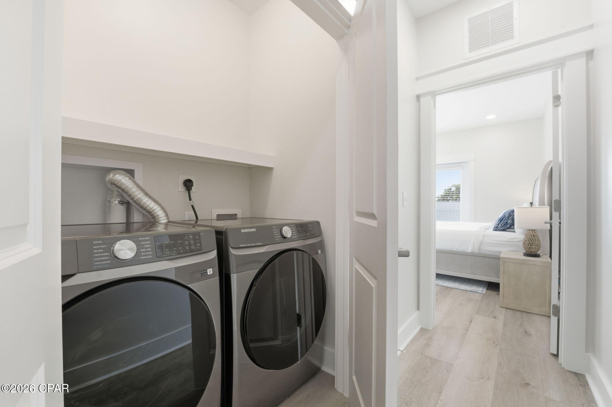 Laundry nook with front-loading washer and dryer, opening onto a bright bedroom.