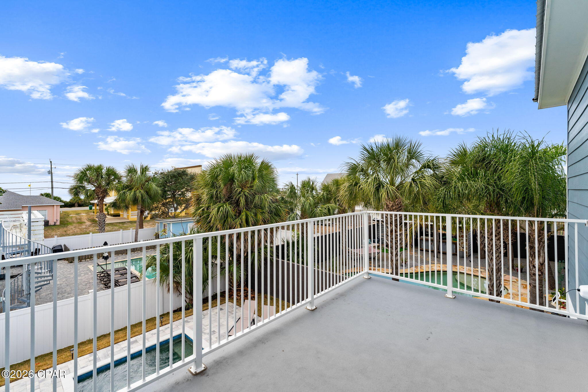 Second-story balcony overlooking a swimming pool and palm-filled backyard.