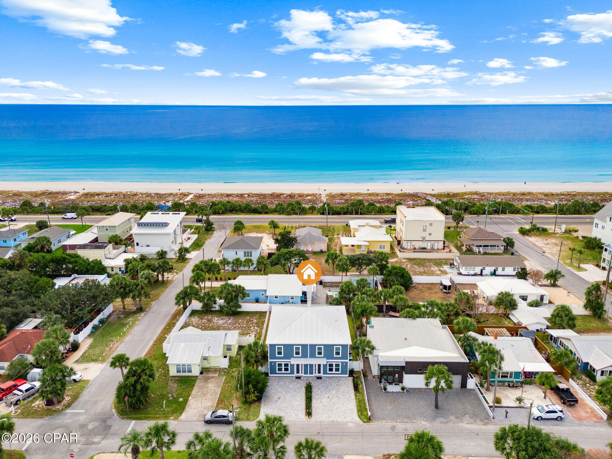 Aerial view of the marked blue home among palm-lined streets, with the beach and Gulf of Mexico beyond.