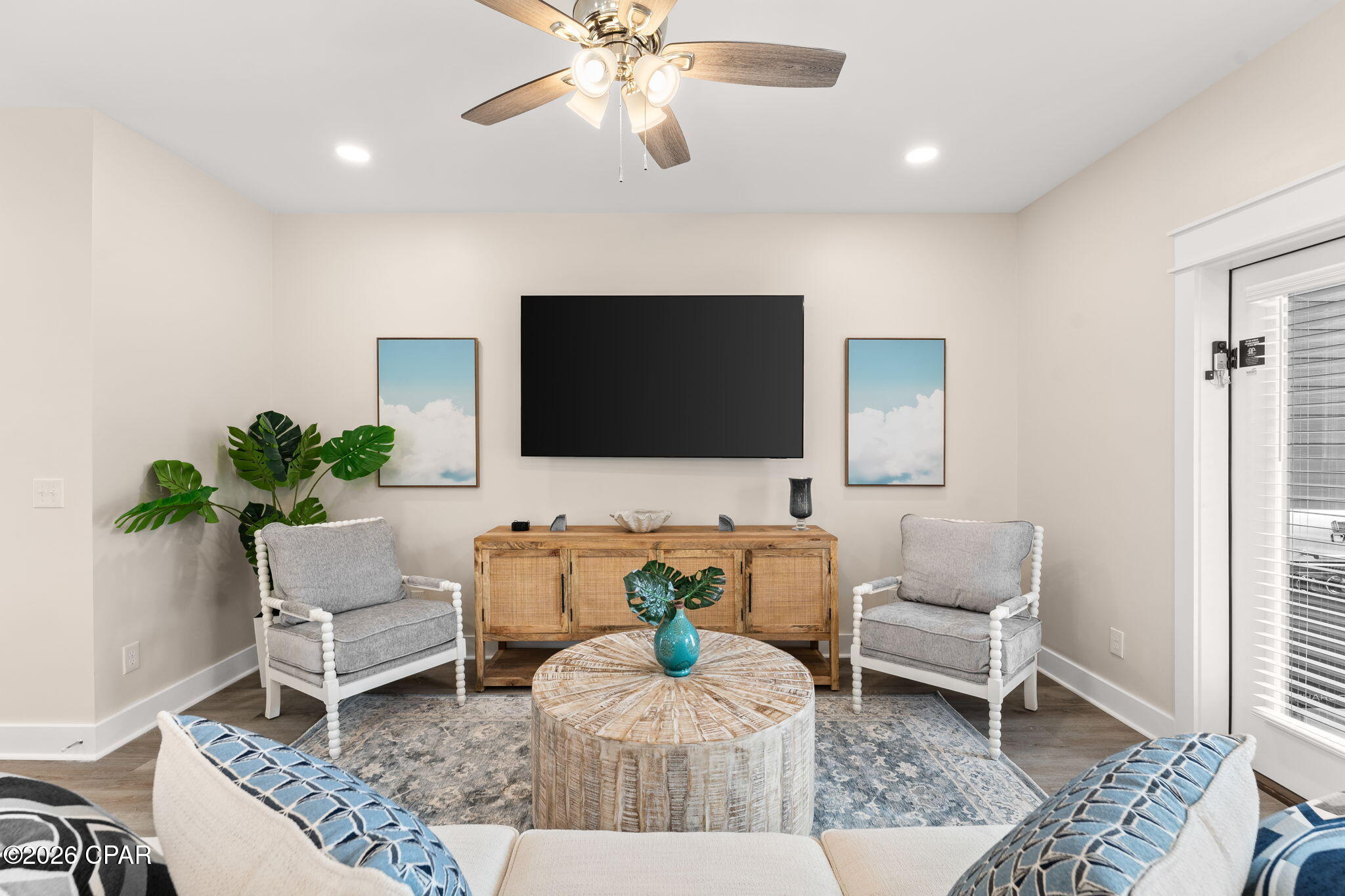 Furnished living room with gray armchairs, wall-mounted television, woven coffee table, and blue patterned rug.