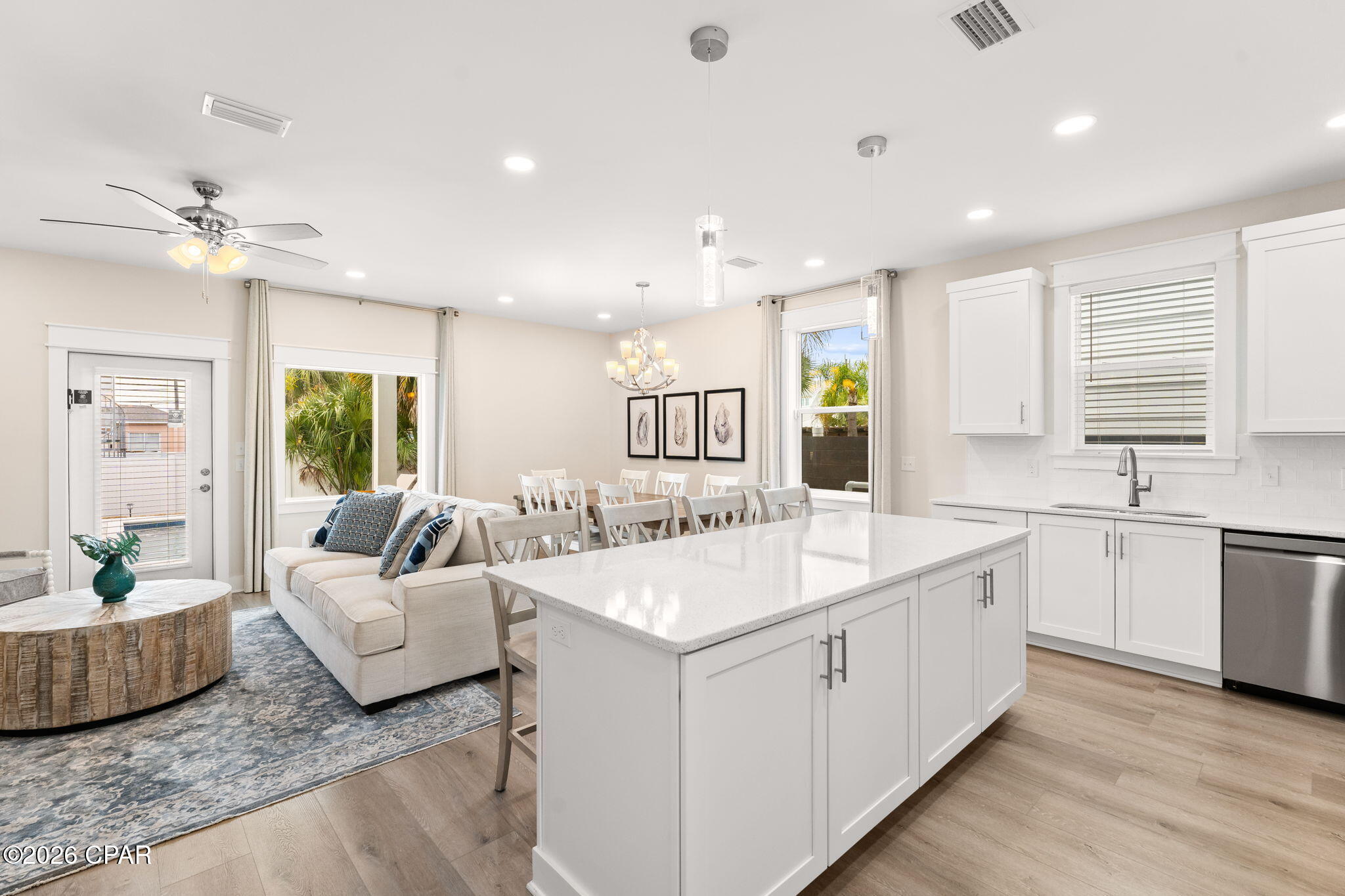 Open-plan kitchen and living area with a large white island, dining table, and palm trees outside.