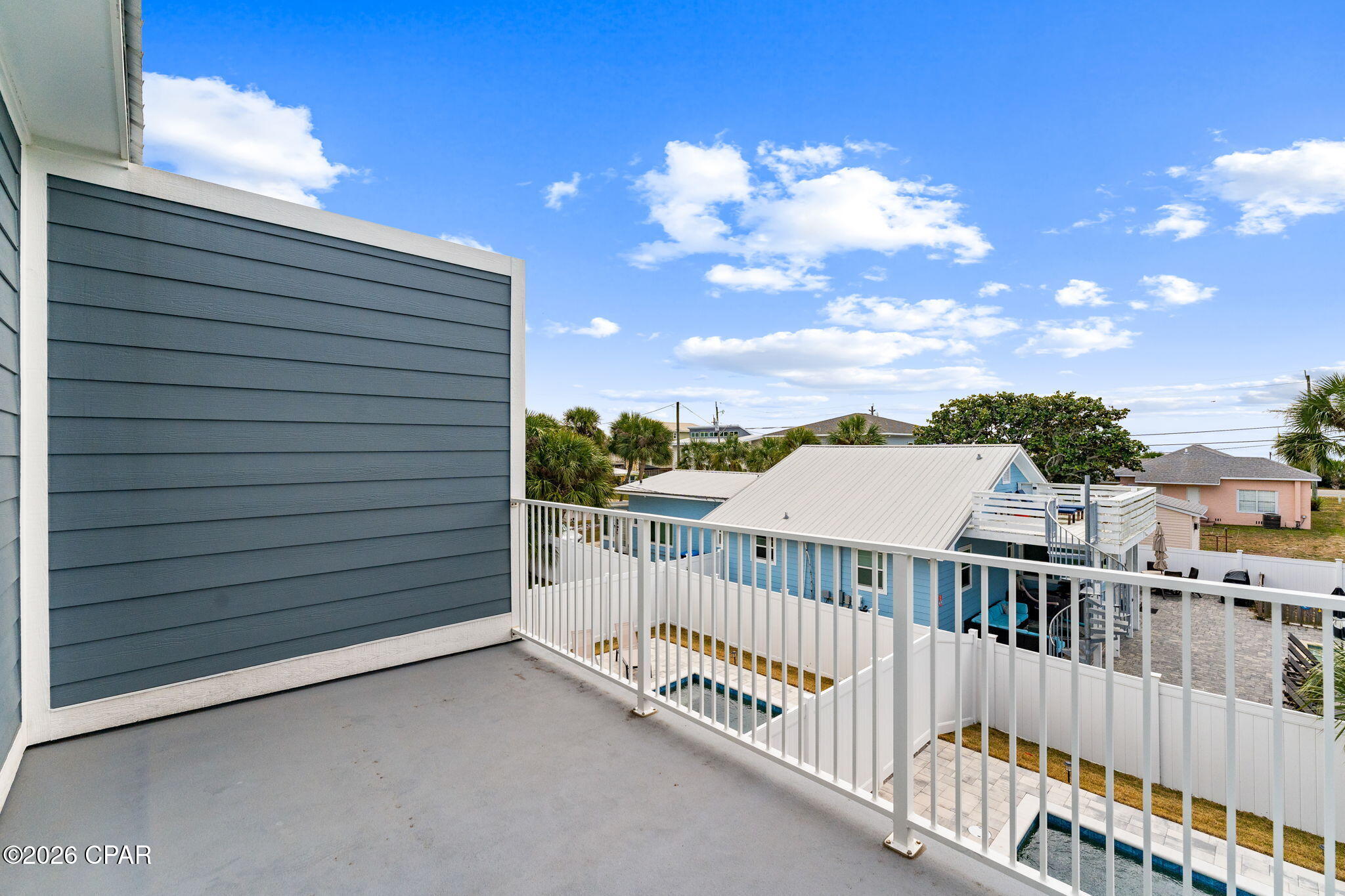 Elevated balcony with white railing overlooking a swimming pool and neighboring homes.