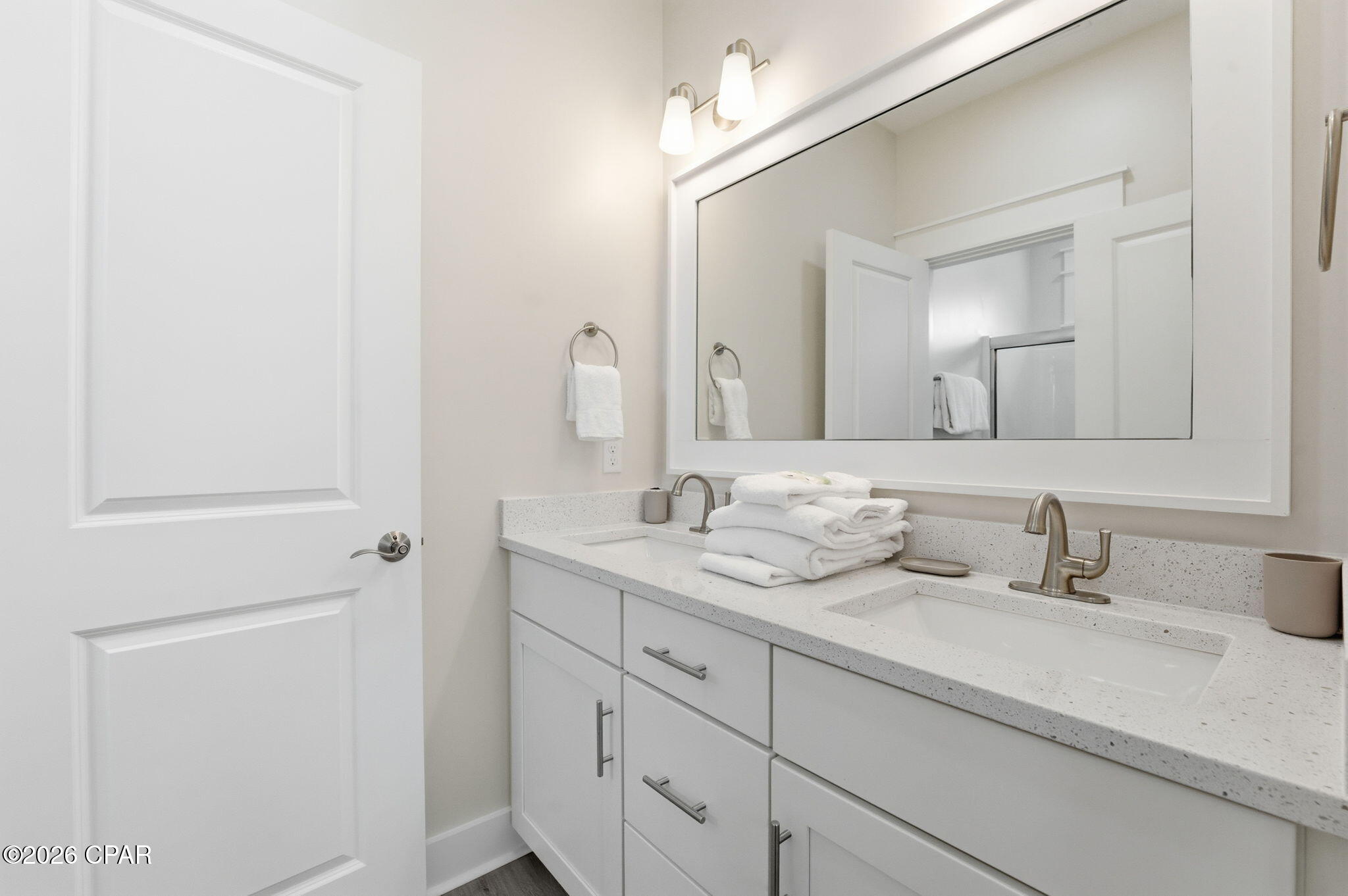 Bathroom with a white double-sink vanity, large mirror, and neatly folded towels.