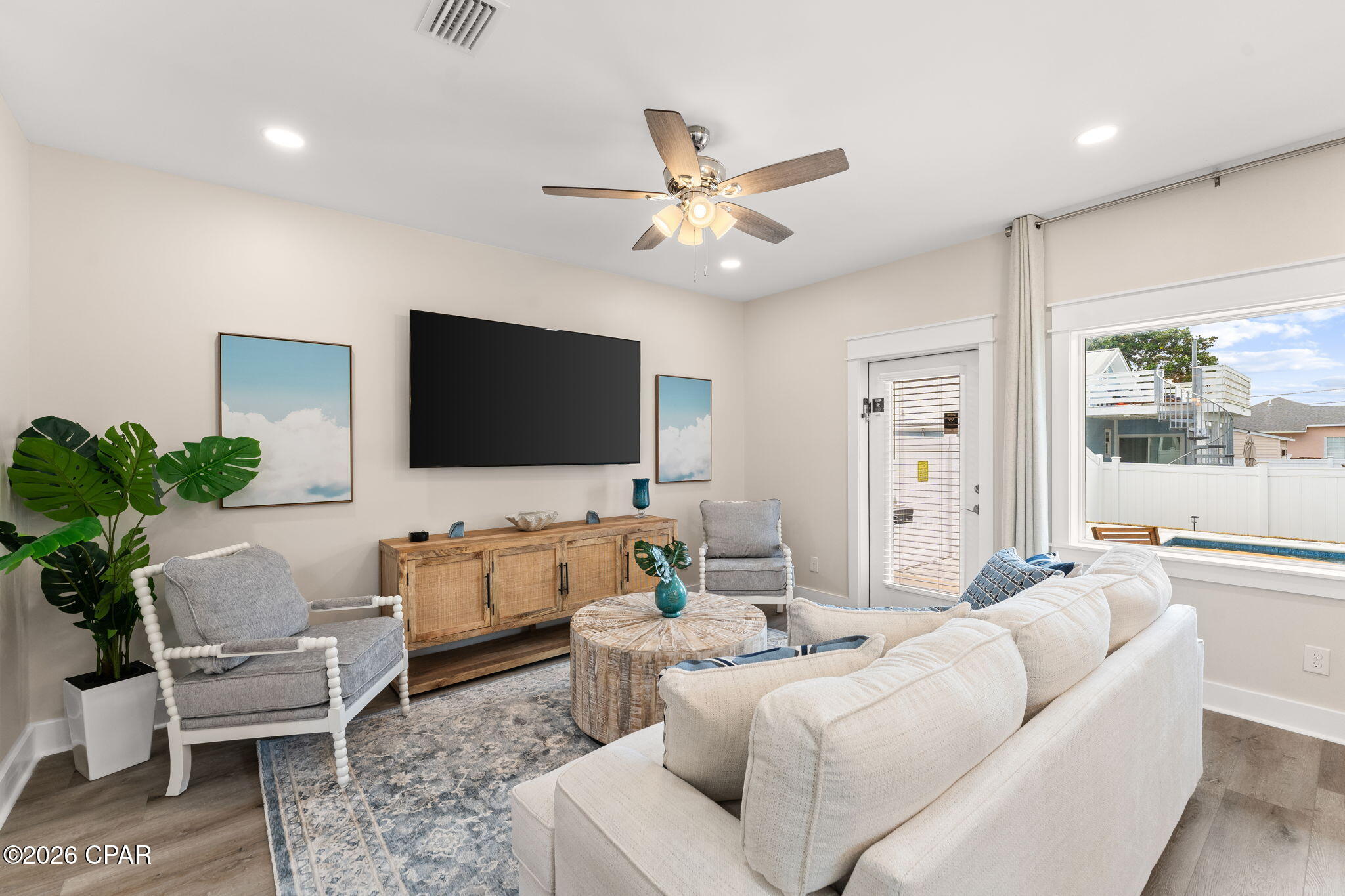 Living room with a white sectional, gray chairs, and a window overlooking a backyard pool.