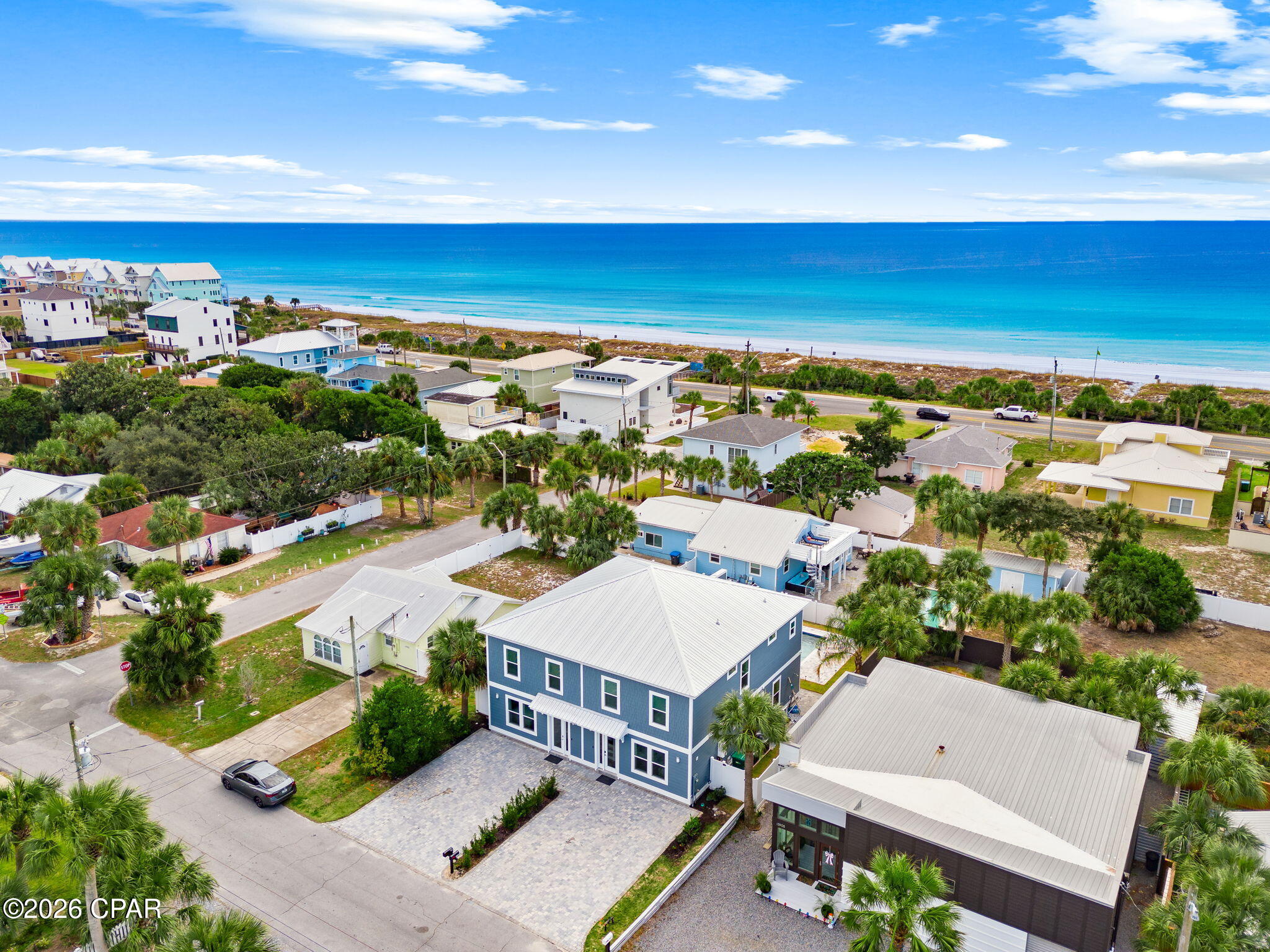 Aerial view of a blue duplex near the beach, with neighboring homes and ocean beyond.