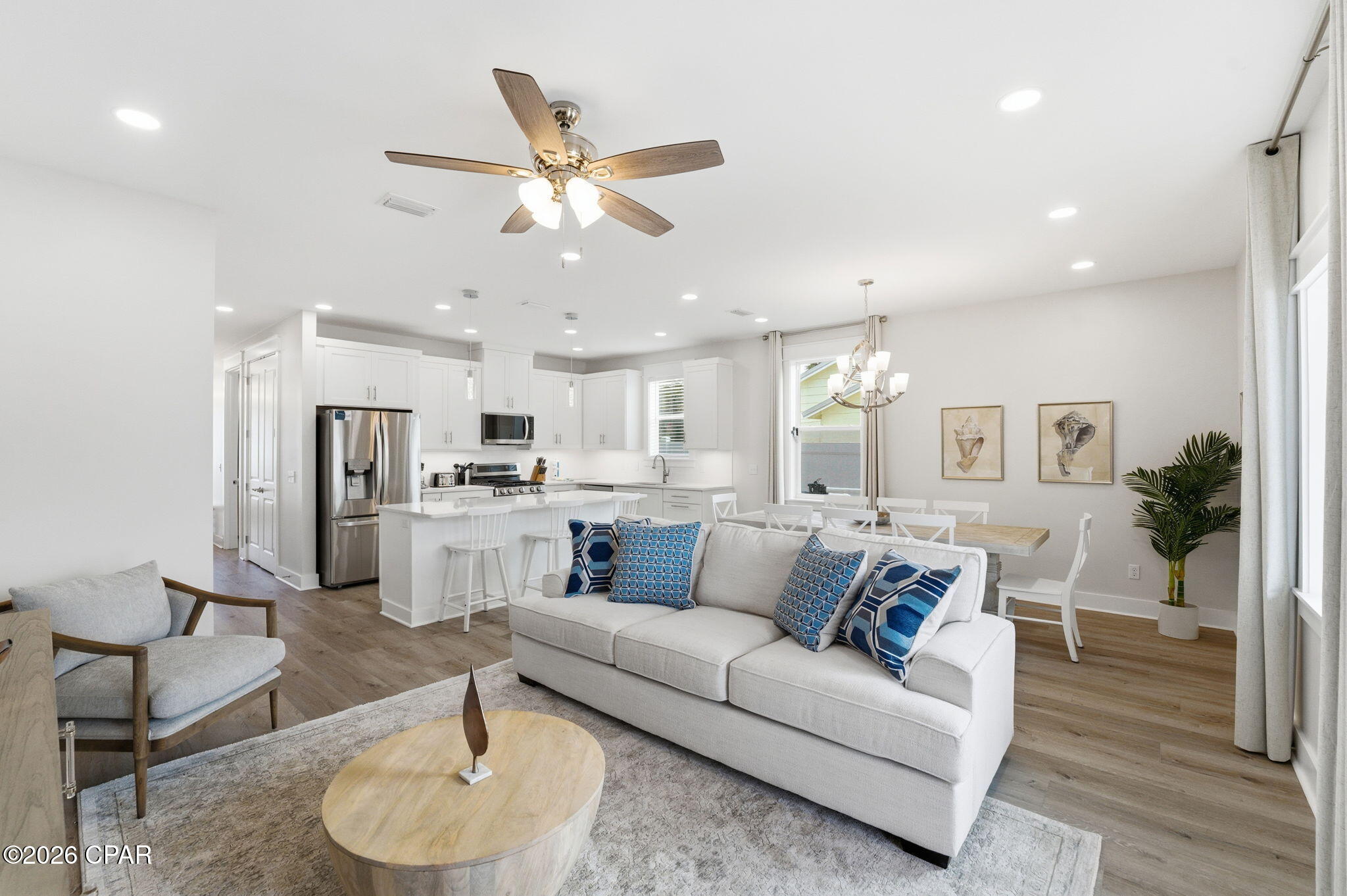 Open-plan living room and kitchen with white furnishings, blue patterned cushions, and wood flooring.
