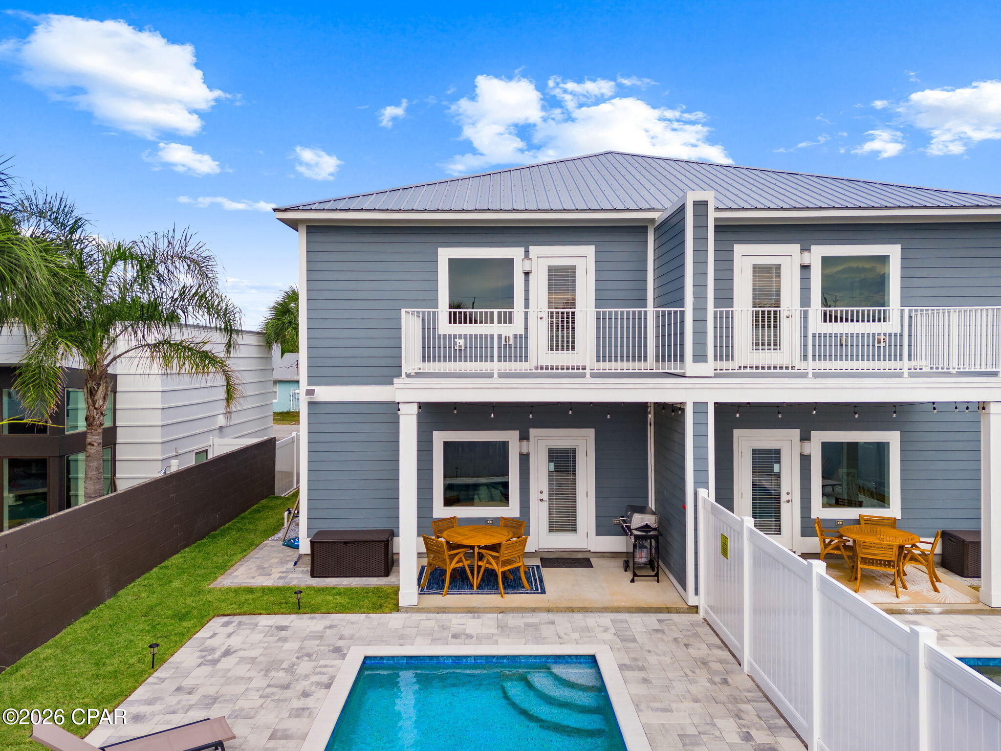 Two-story duplex with white-railed balconies, patio dining areas, and a swimming pool.