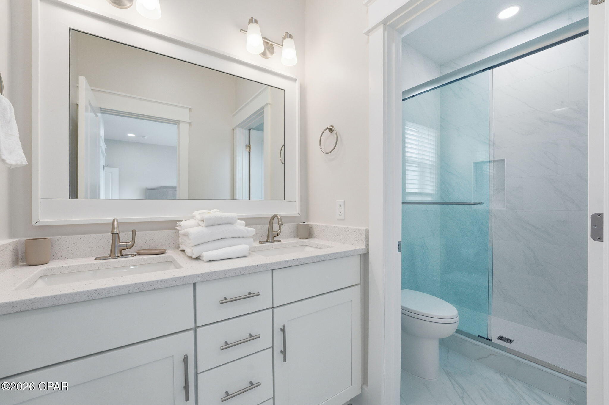 Bright bathroom with a white double vanity and glass-enclosed shower.