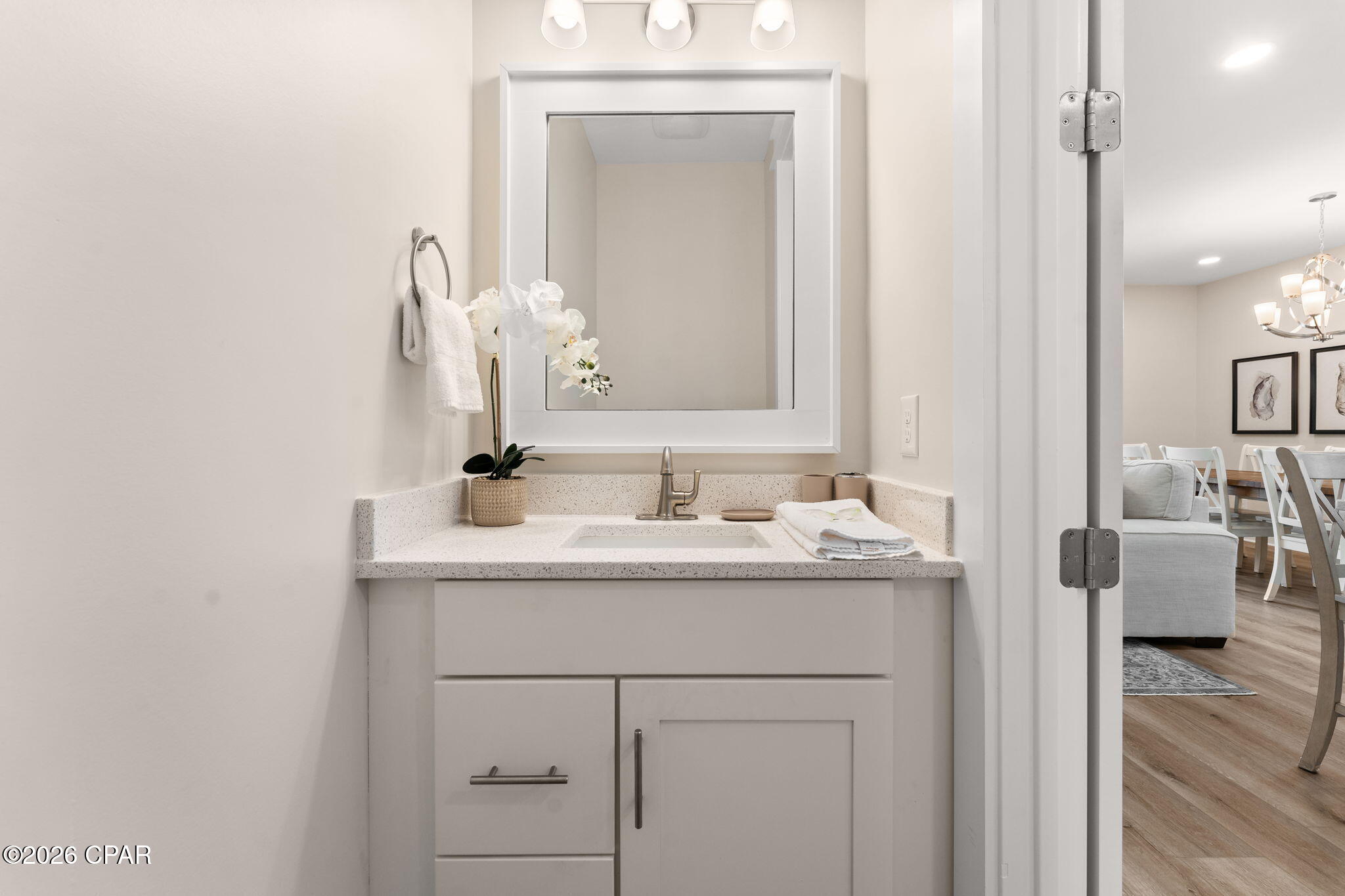 Bathroom vanity with a framed mirror, speckled countertop, sink, and orchid beside an open doorway.