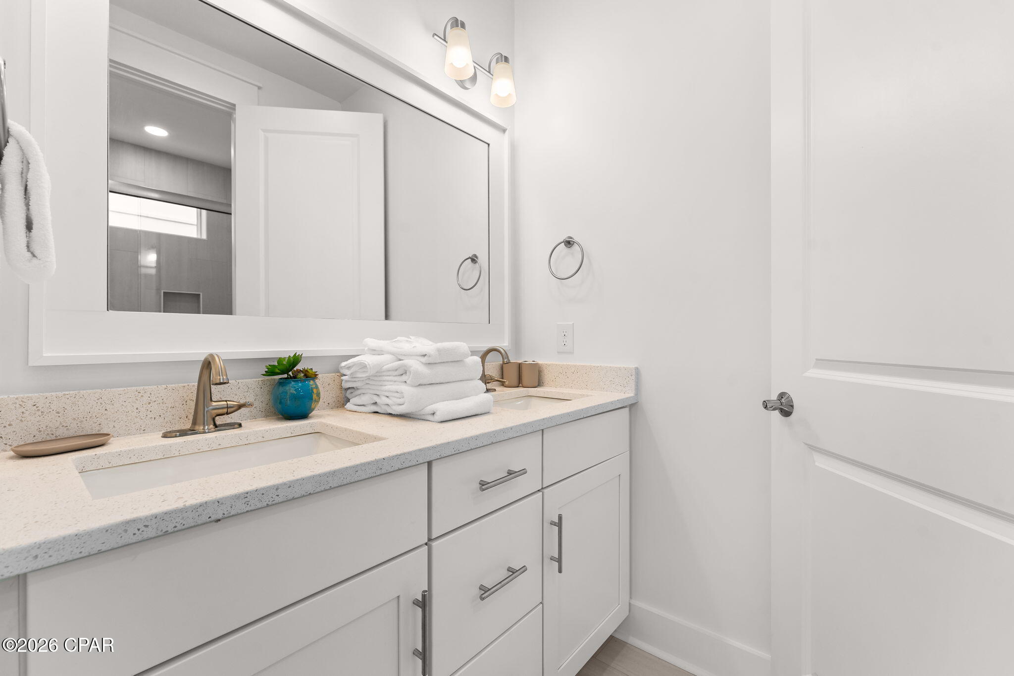 Bathroom vanity with a large mirror, speckled countertop, double sinks, and folded white towels.
