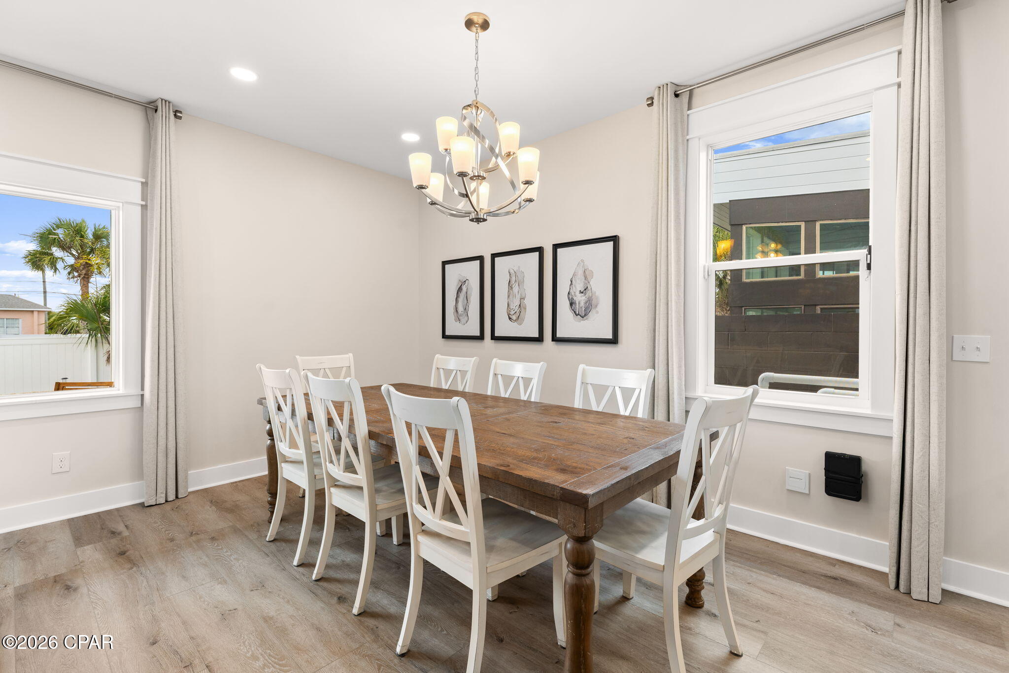 Dining room with a rustic wooden table, white chairs, and a modern chandelier.