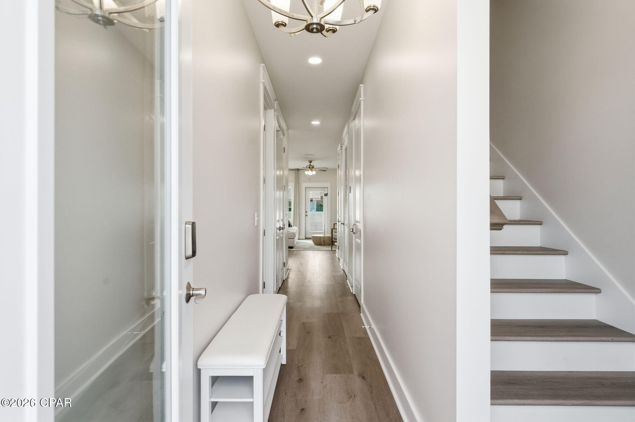 Bright hallway with wood-look floors, a white entry bench, and stairs along one side.