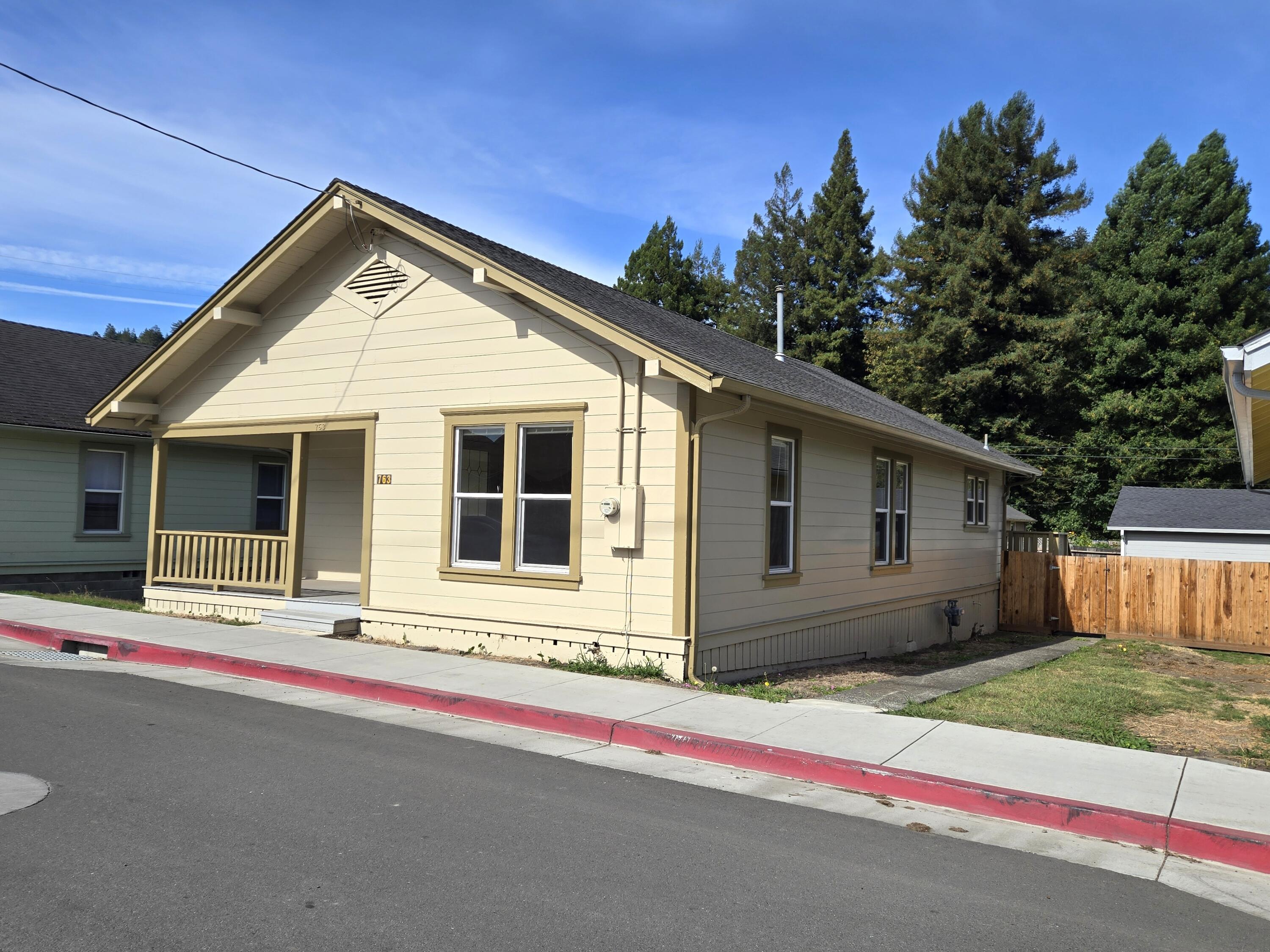 Cream-colored single-story house with a covered porch, front windows, and wooden fence.
