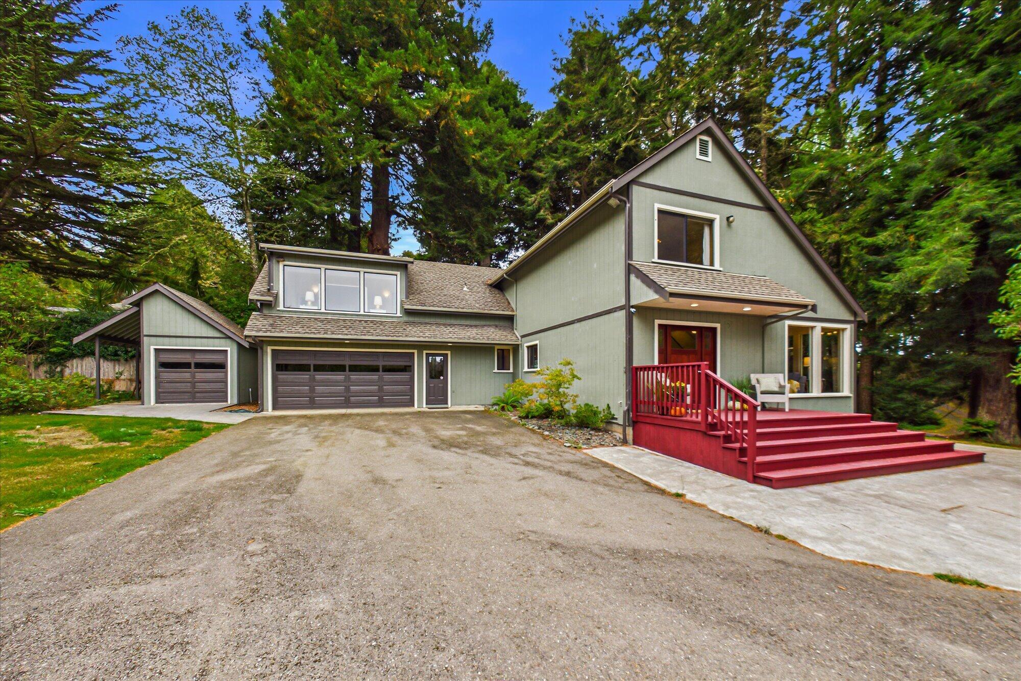 Gray-green home with a large garage and red front porch, surrounded by tall trees.