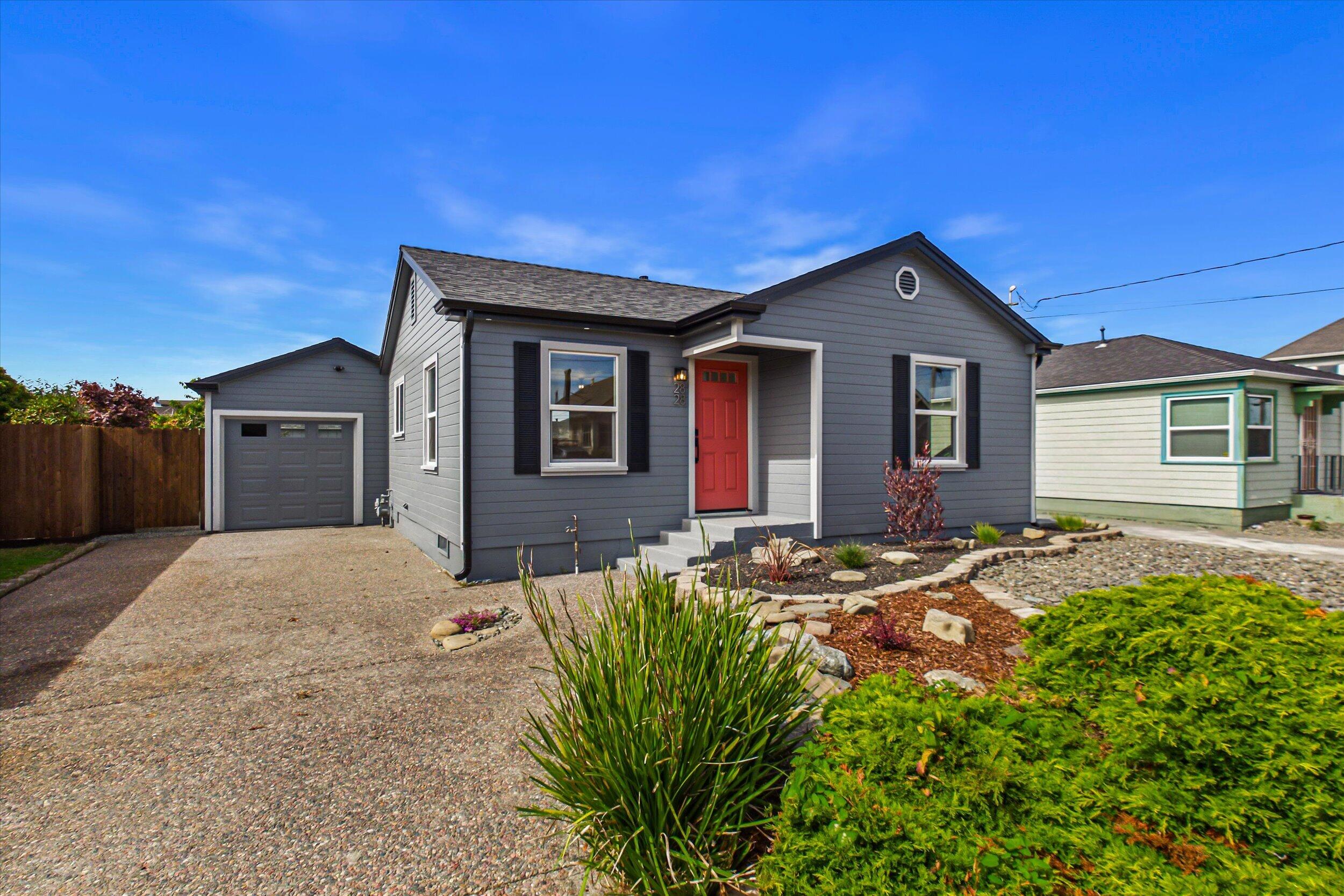 Gray single-story home with a red front door, attached garage, and landscaped garden.