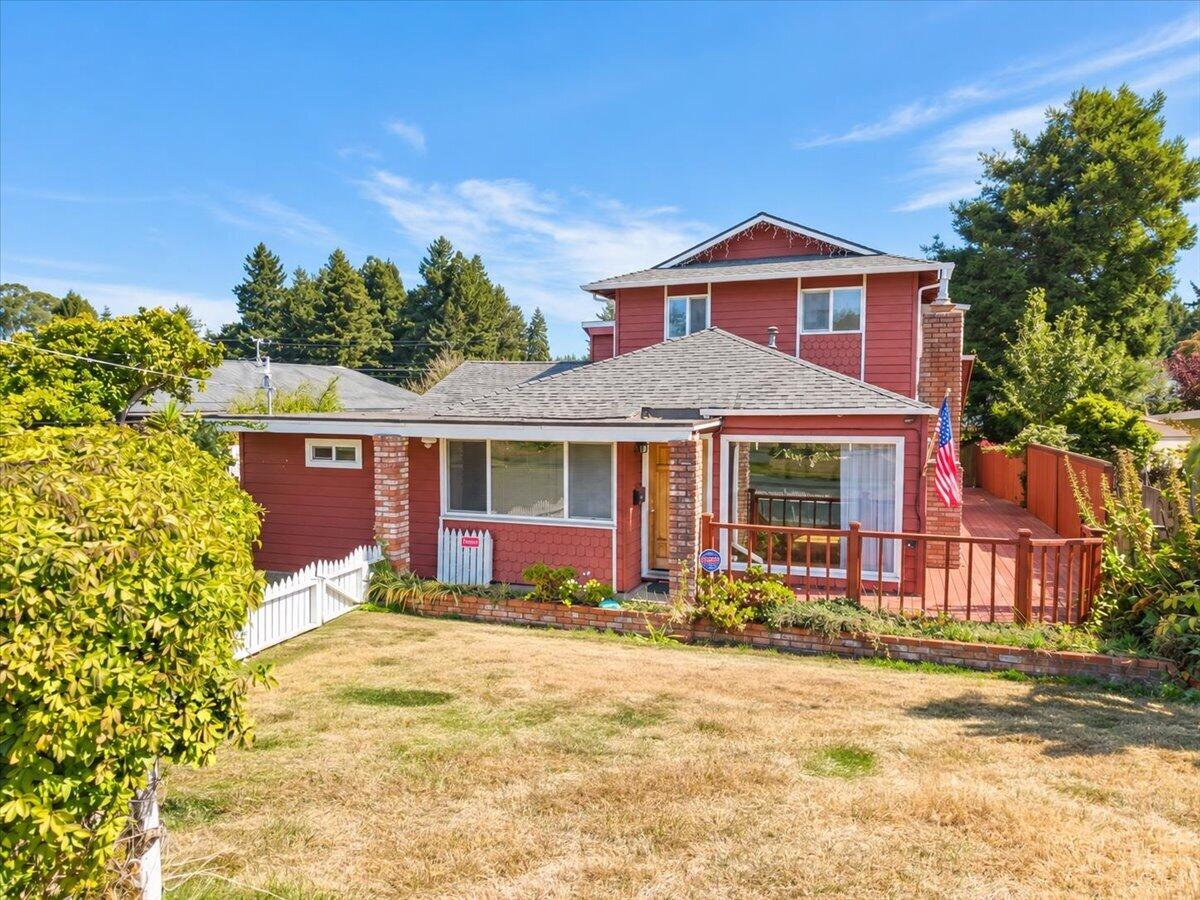 Red two-story house with brick accents, a raised deck, and a white picket fence.
