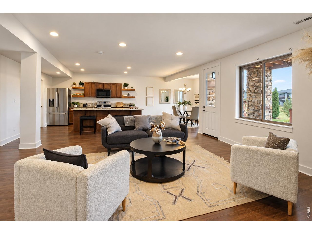 Open-concept living room and kitchen with a gray sofa, cream chairs, and dark wood cabinetry.