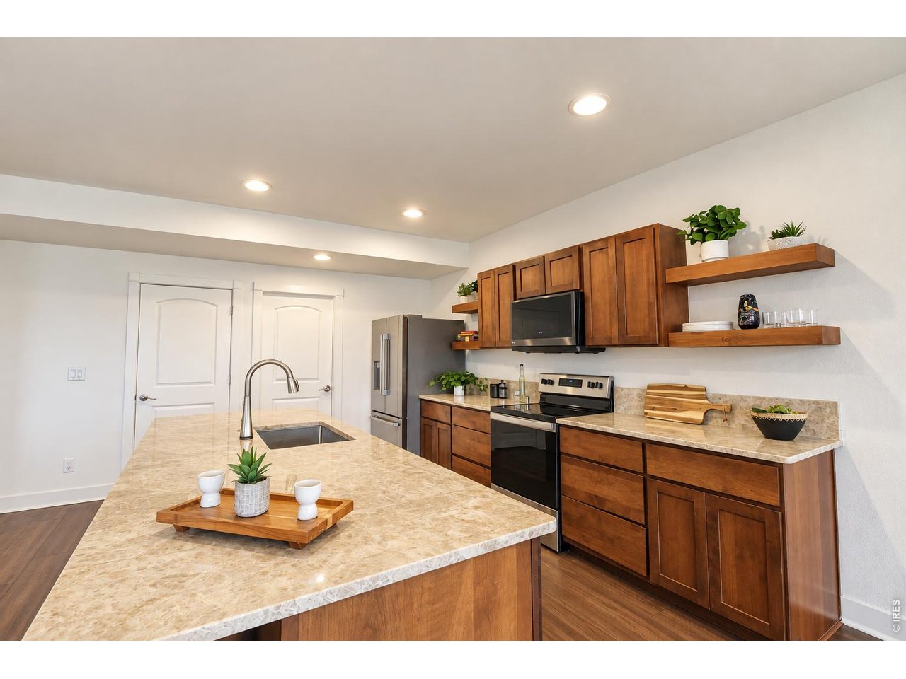 Kitchen with warm wood cabinets, stone counters, stainless steel appliances, and a large island sink.