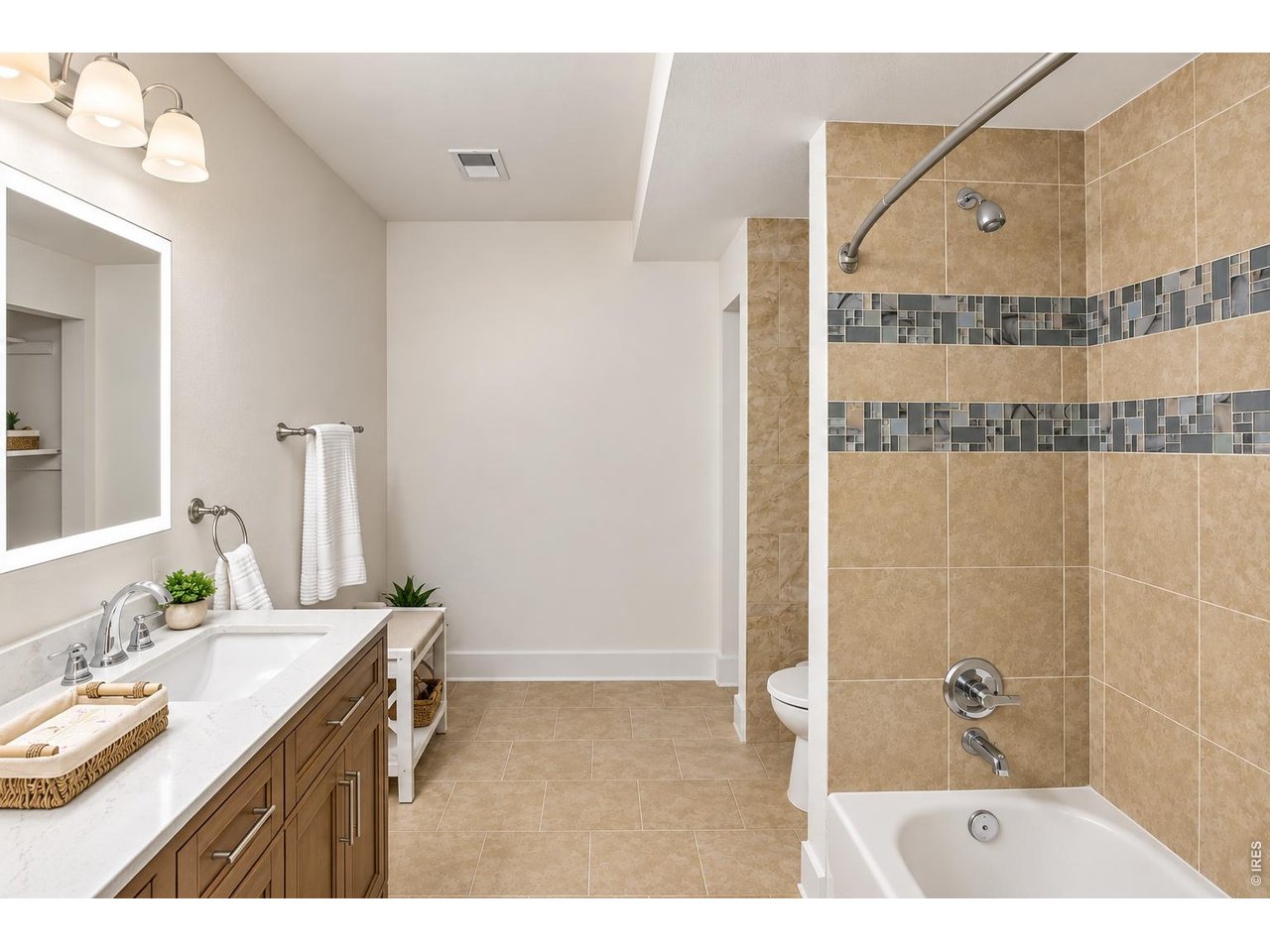Bathroom with a wood vanity and a bathtub surrounded by tan tile and mosaic accents.