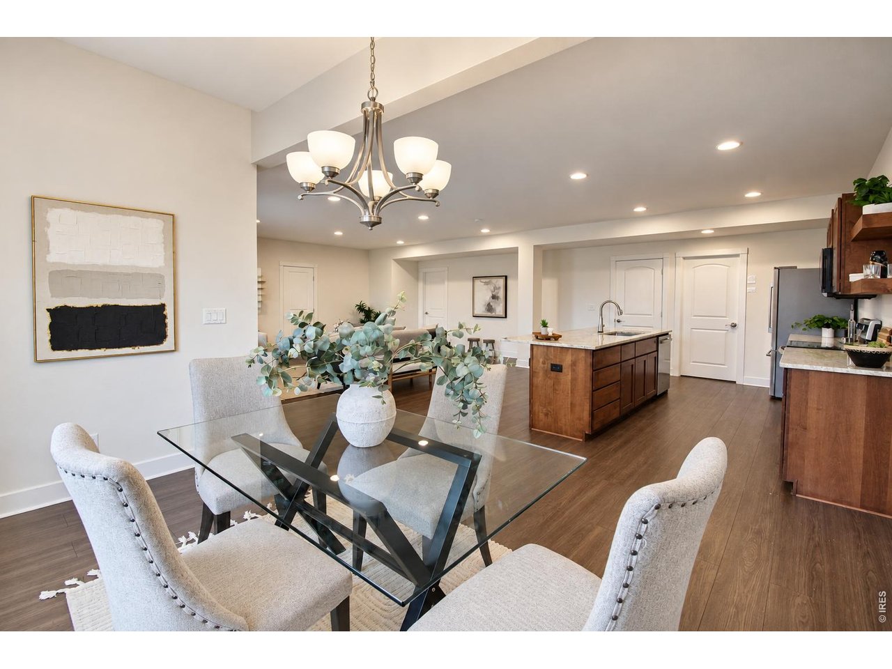 Dining room with a glass-top table and upholstered chairs beside an open kitchen and wood island.