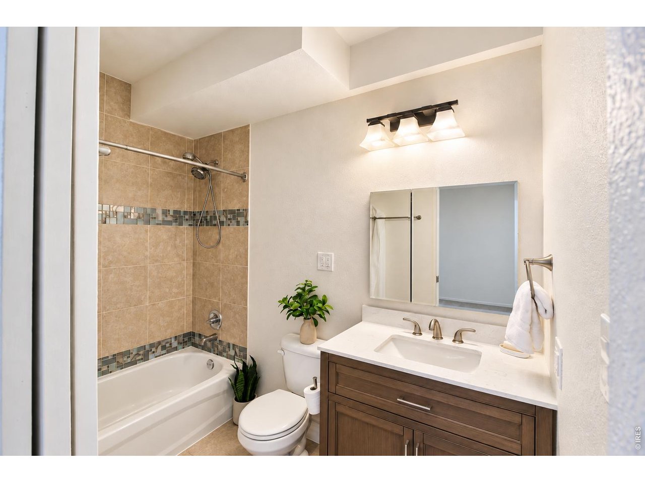 Bathroom with a tiled tub surround, mosaic accents, and a wood vanity.