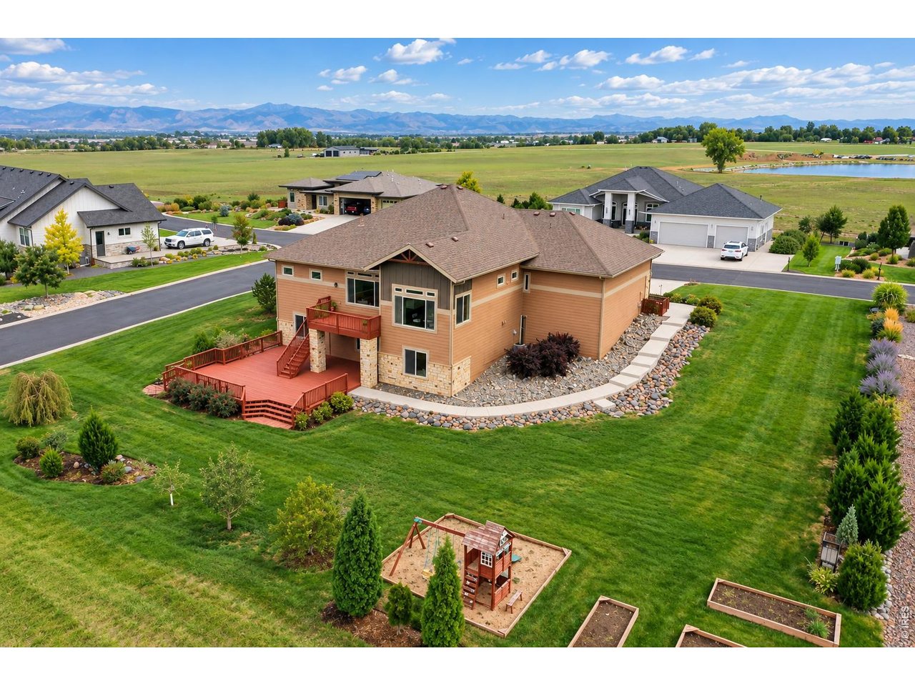 Aerial view of a two-story home with a large red deck, landscaped yard, and mountains in the distance.