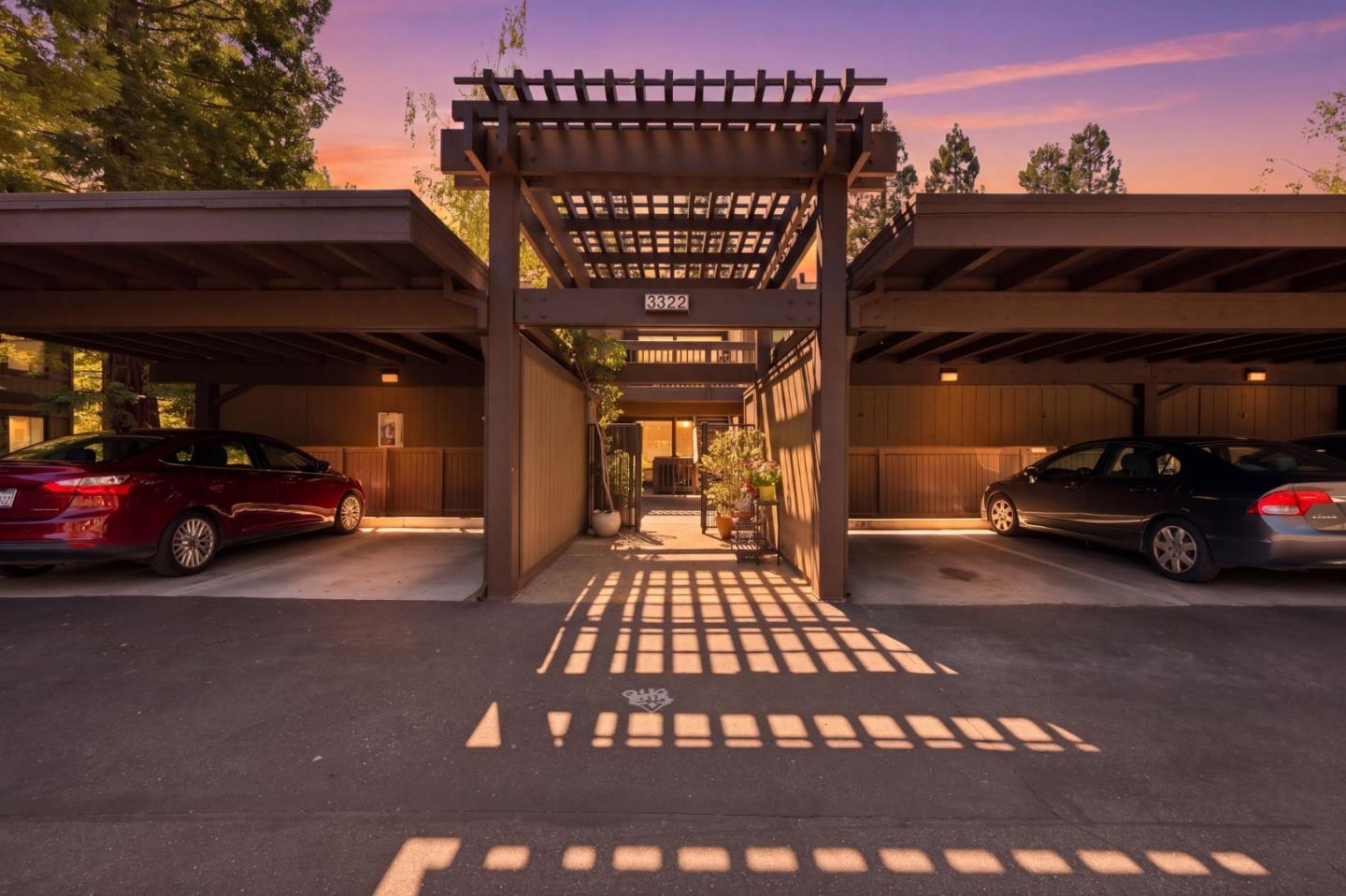 Property entrance with a wooden pergola walkway and covered parking bays at sunset.