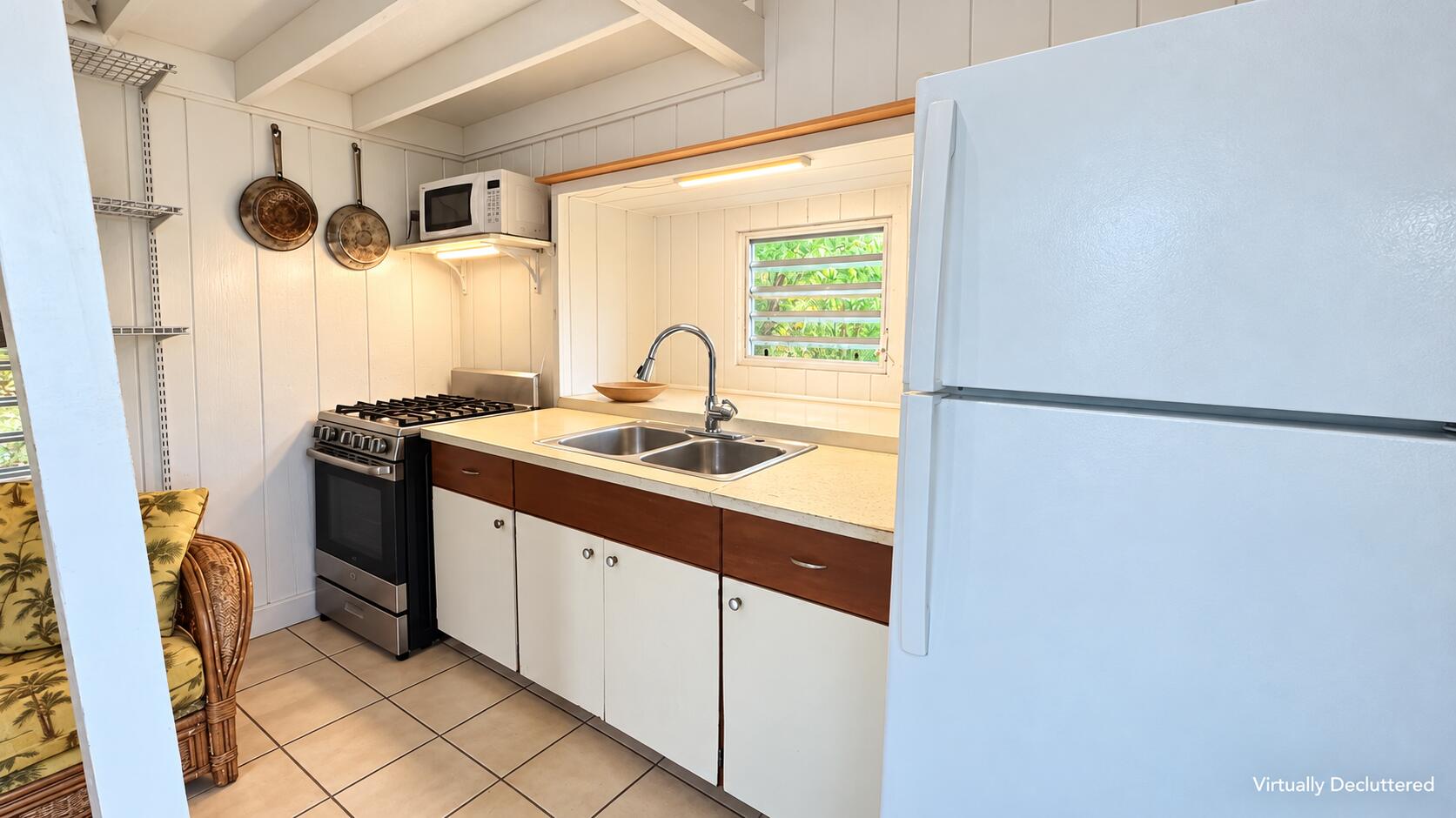Compact white kitchen with a double-basin sink, gas range, and louvered window overlooking greenery.