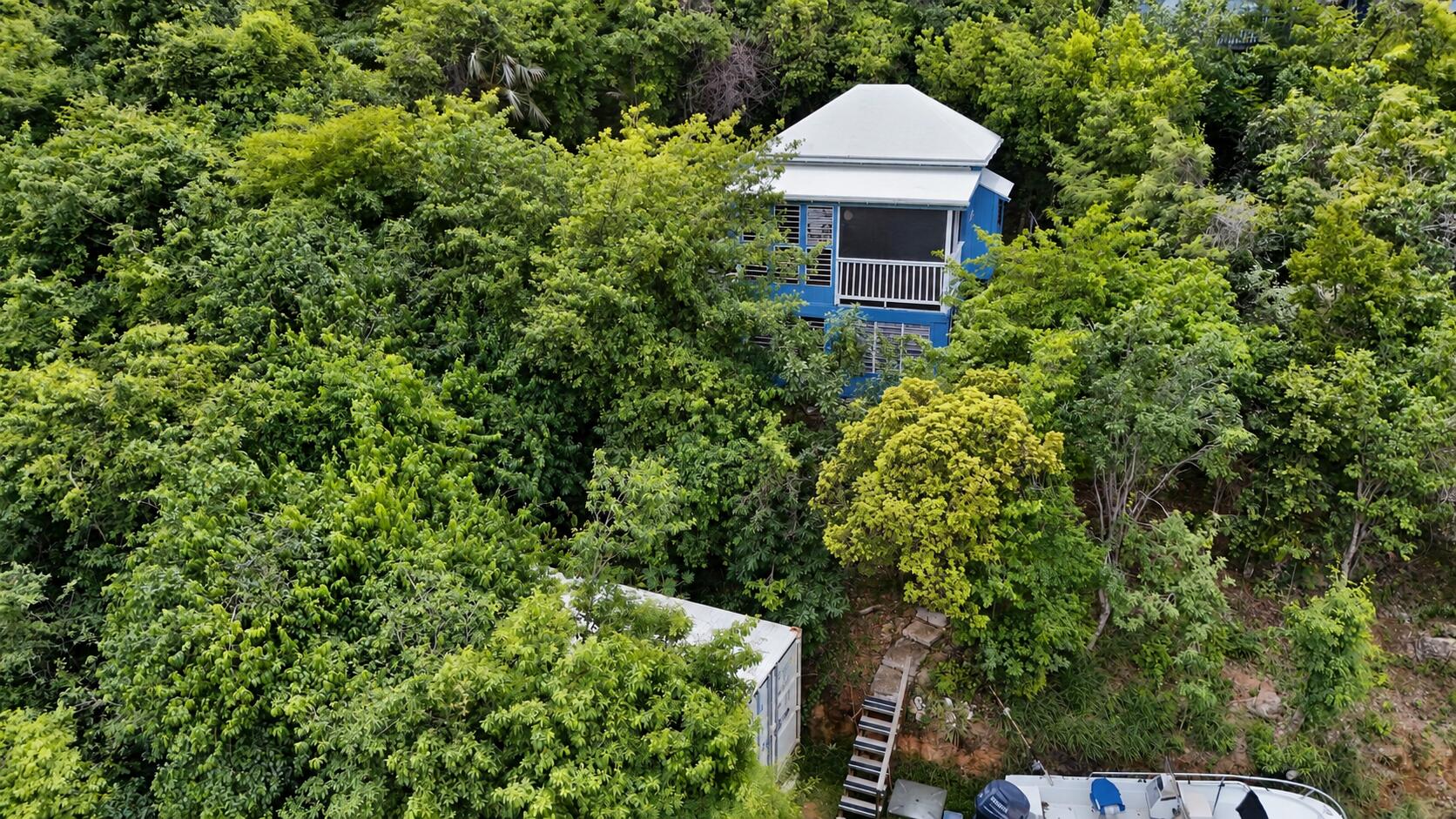 Blue house nestled in dense tropical greenery, with stairs and a boat below.
