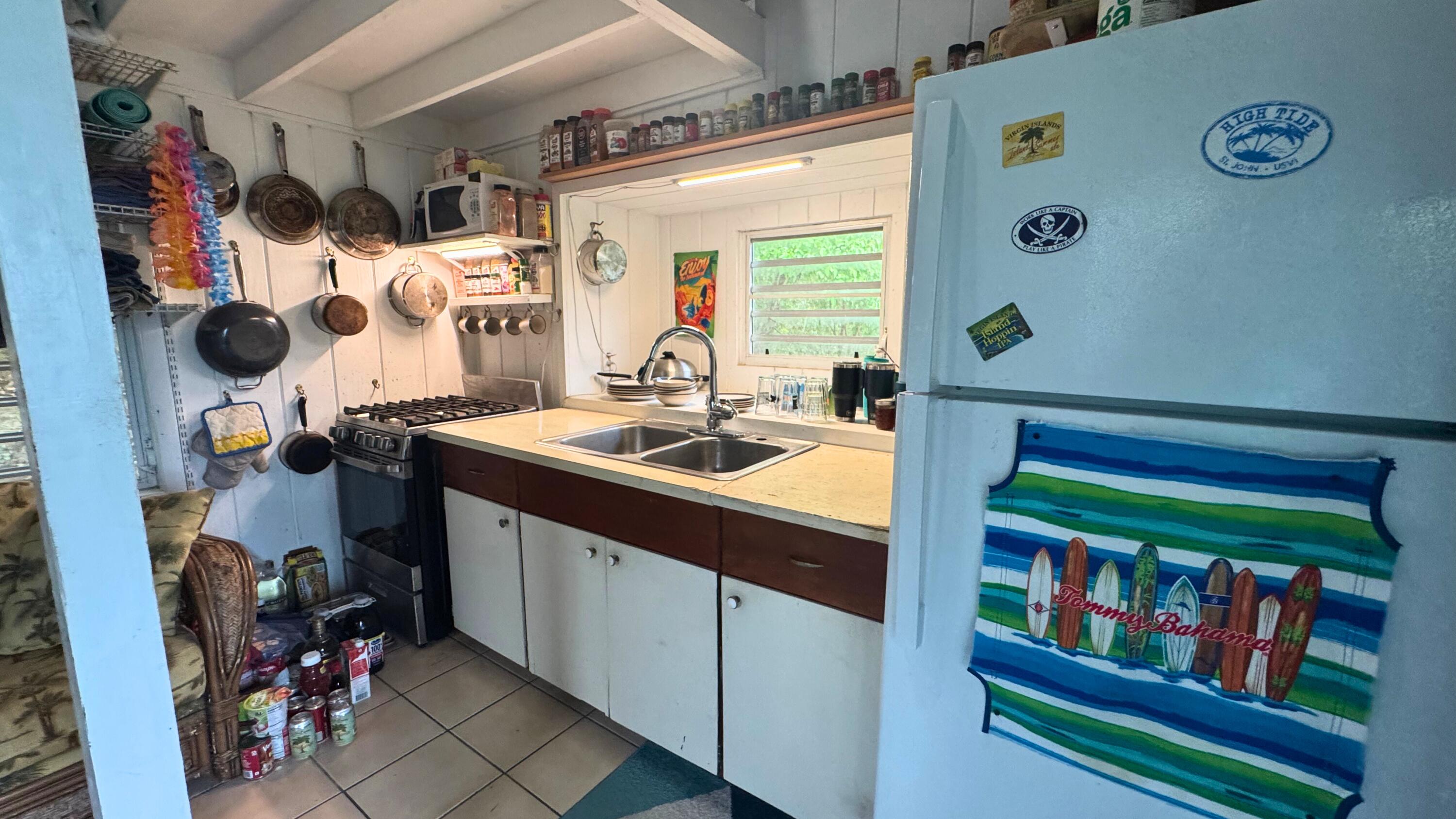 Compact kitchen with hanging cookware, a gas range, double sink, and a magnet-covered refrigerator.