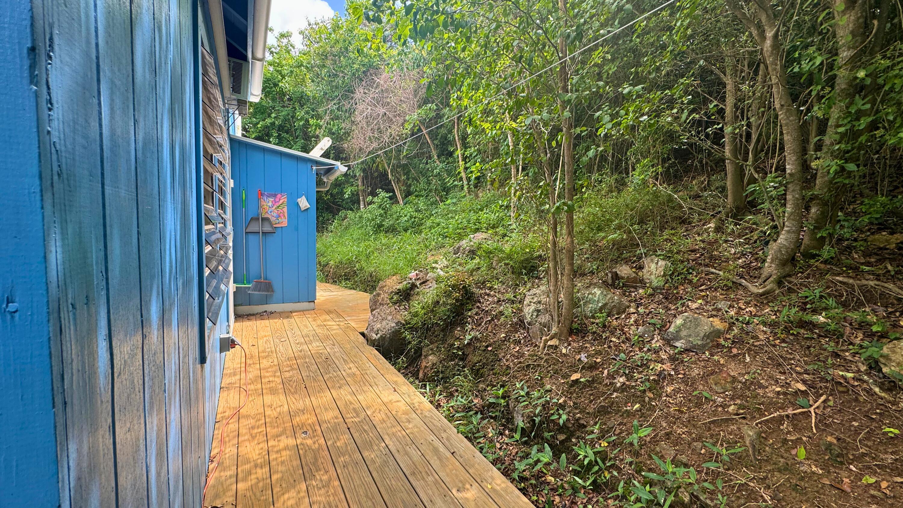 Wooden deck beside a blue-sided house and a densely wooded hillside.
