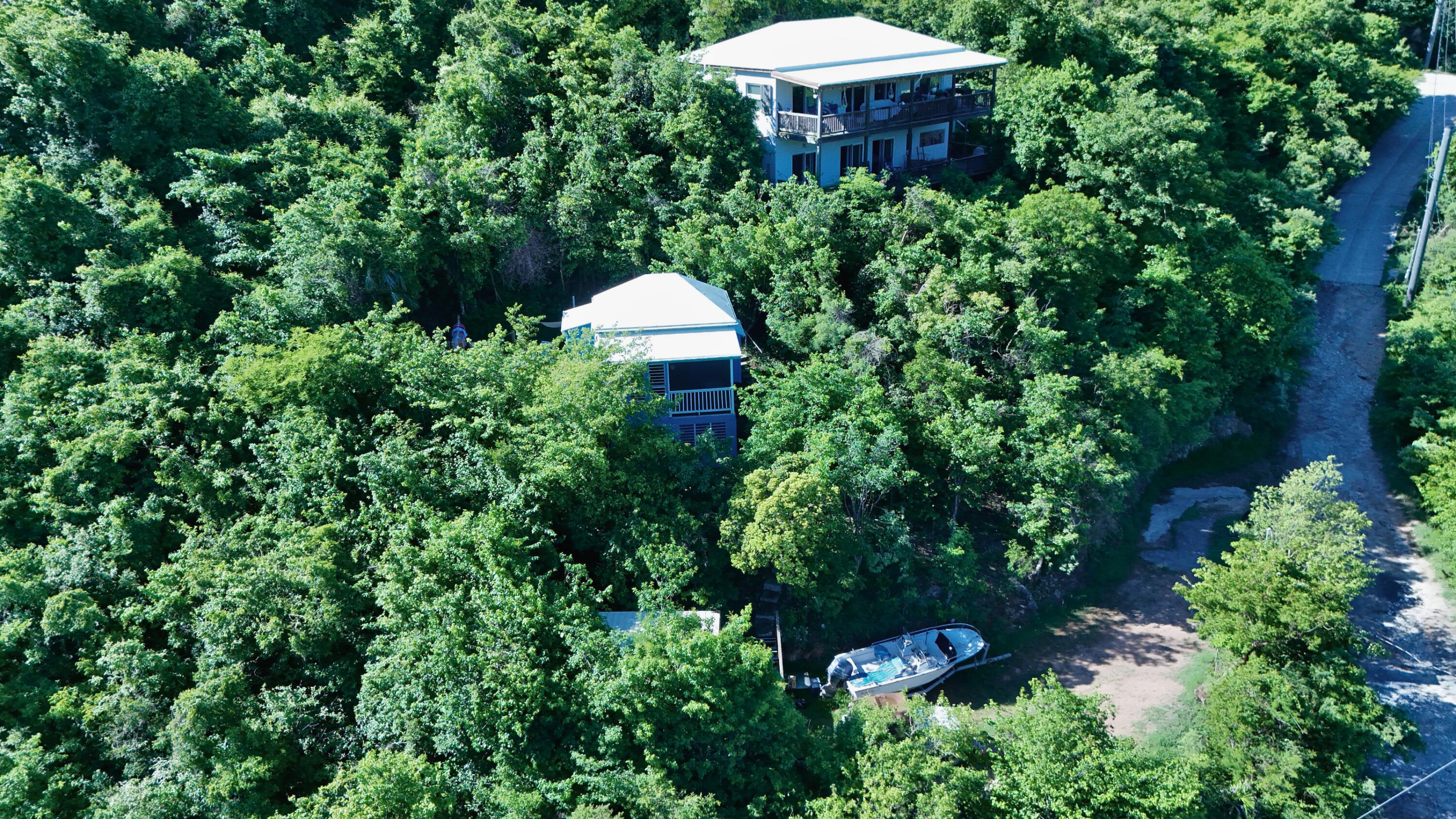 Aerial view of two homes nestled in dense greenery, with a boat beside a clearing.