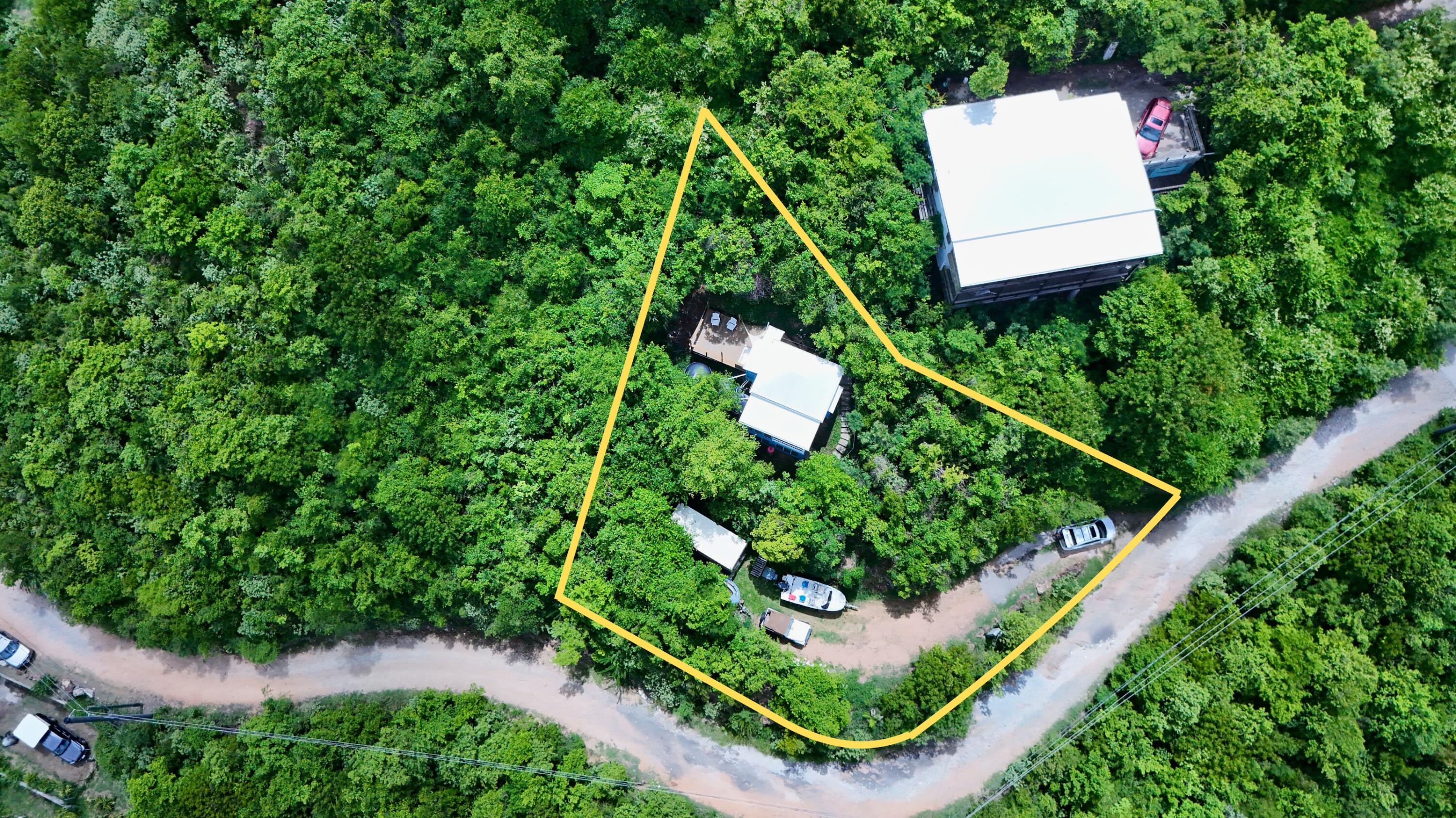 Aerial view of a wooded property outlined in yellow, with several buildings beside a dirt road.