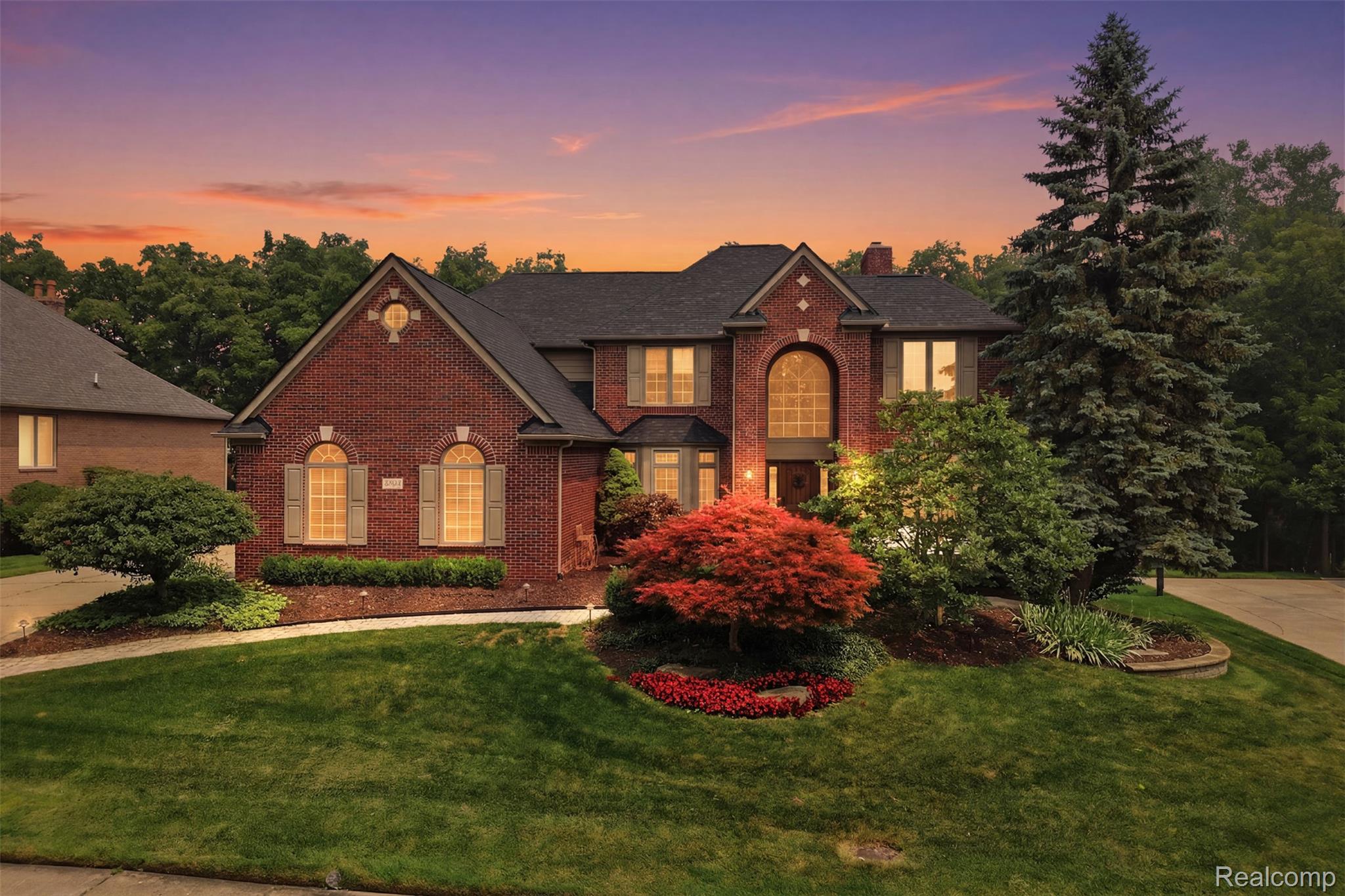 Red-brick house at dusk with arched windows and a landscaped front yard.